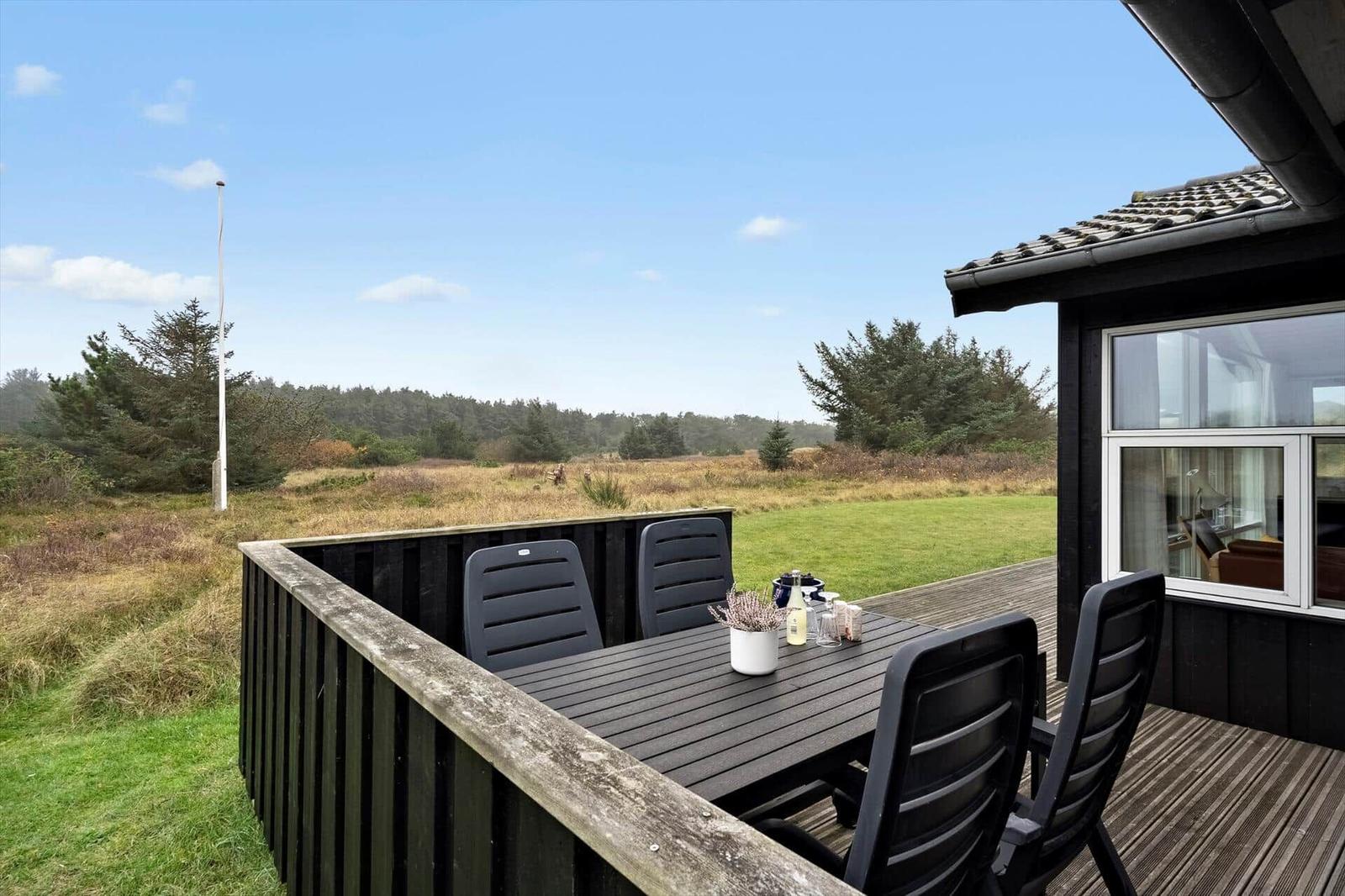 Terrasse mit Tisch und Stühlen, Blick auf Wiese und Wald.