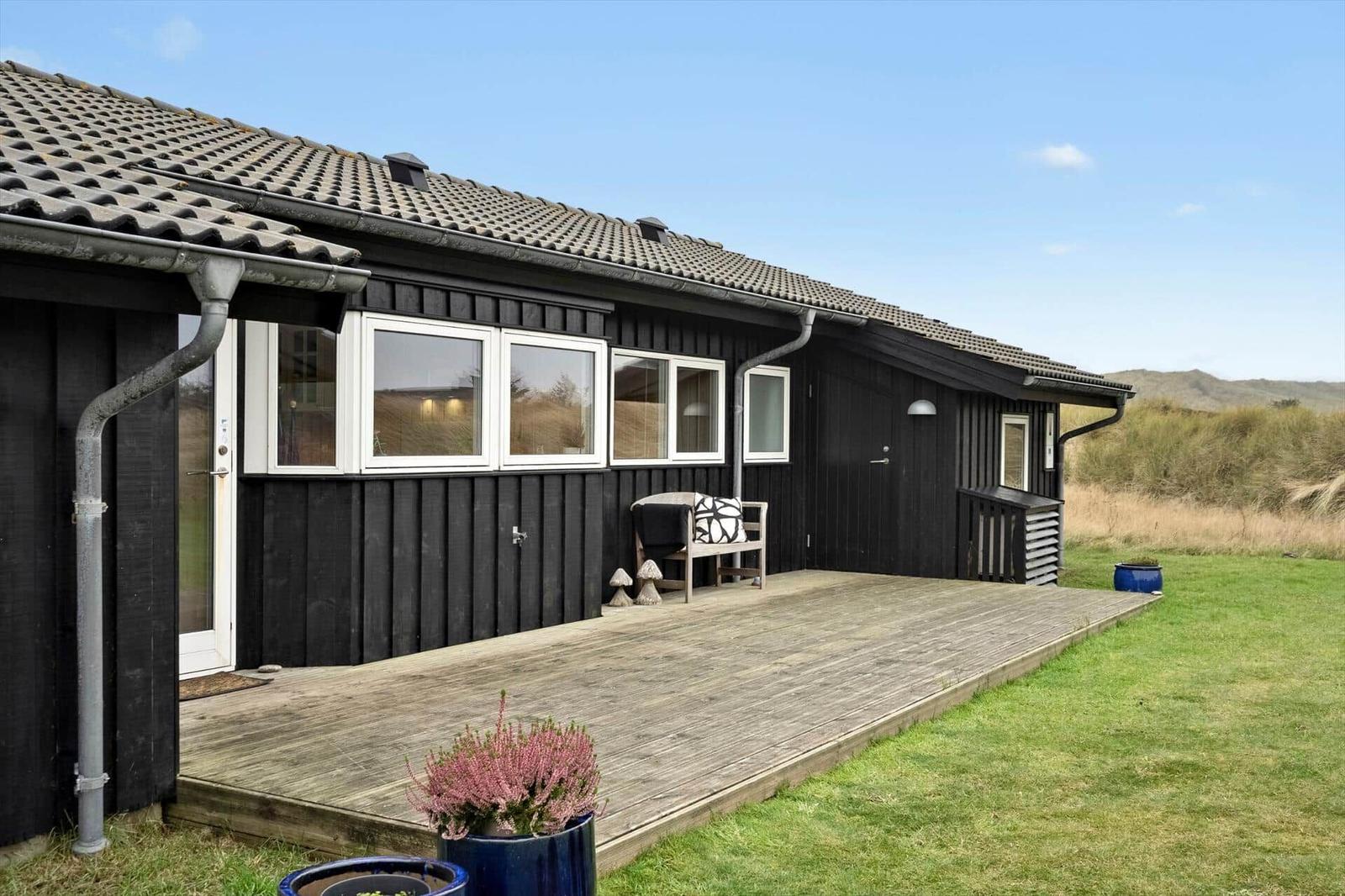 Schwarzes Holzhaus mit Terrasse und Garten. Fenster und Tür sind weiß.
