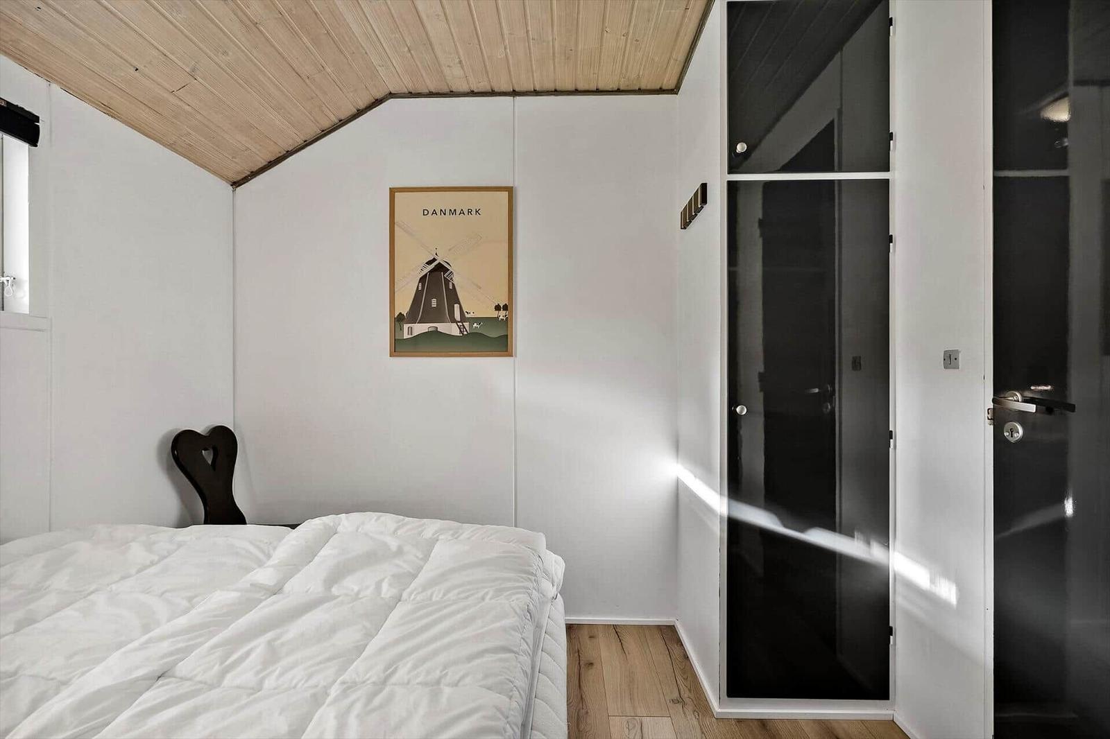 Schlafzimmer mit Bett, Holzdecke und Kleiderschrank. Wandbild zeigt Windmühle in Dänemark.
