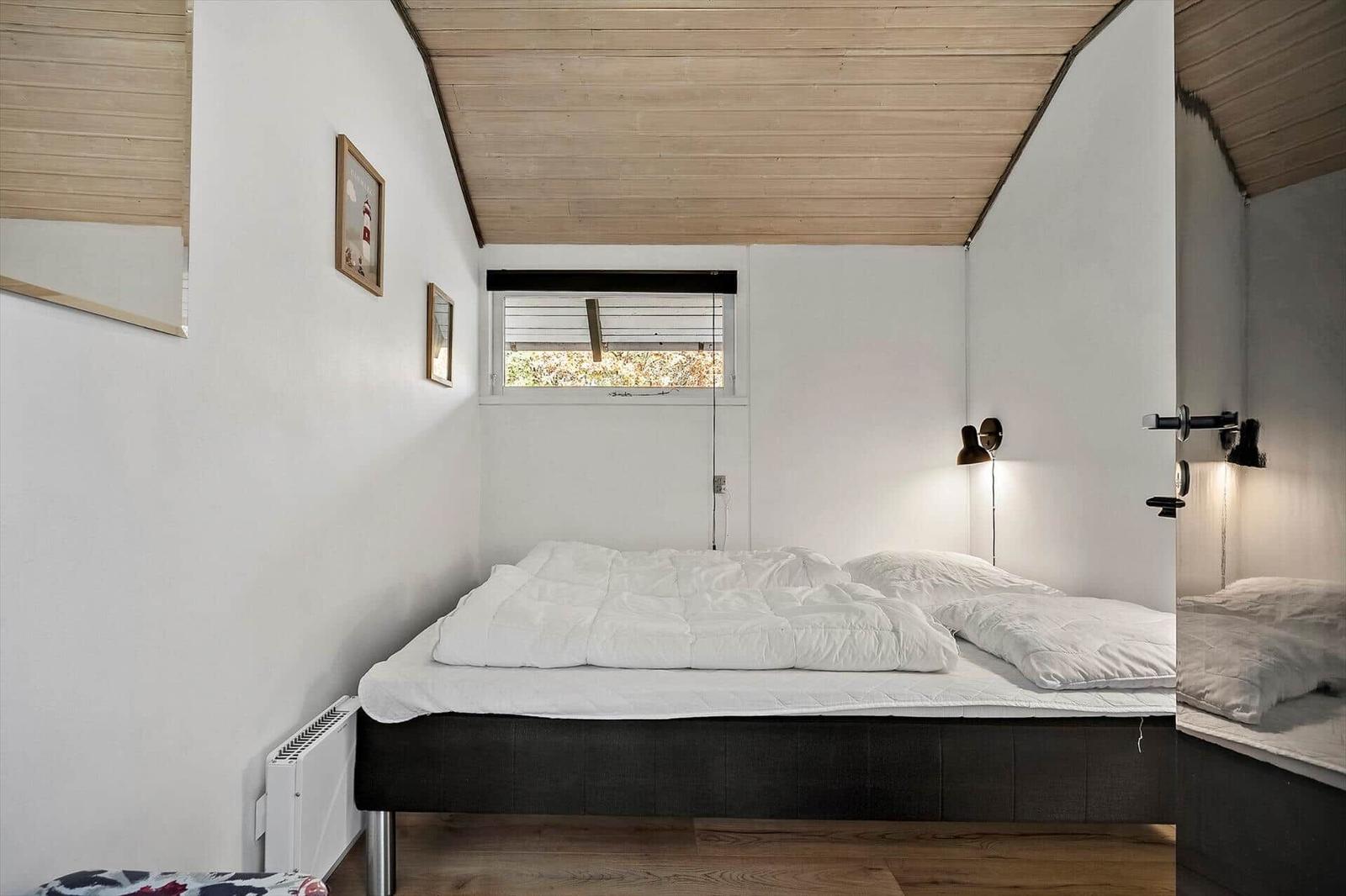 Schlafzimmer mit Bett, Fenster und Holzdecke.
