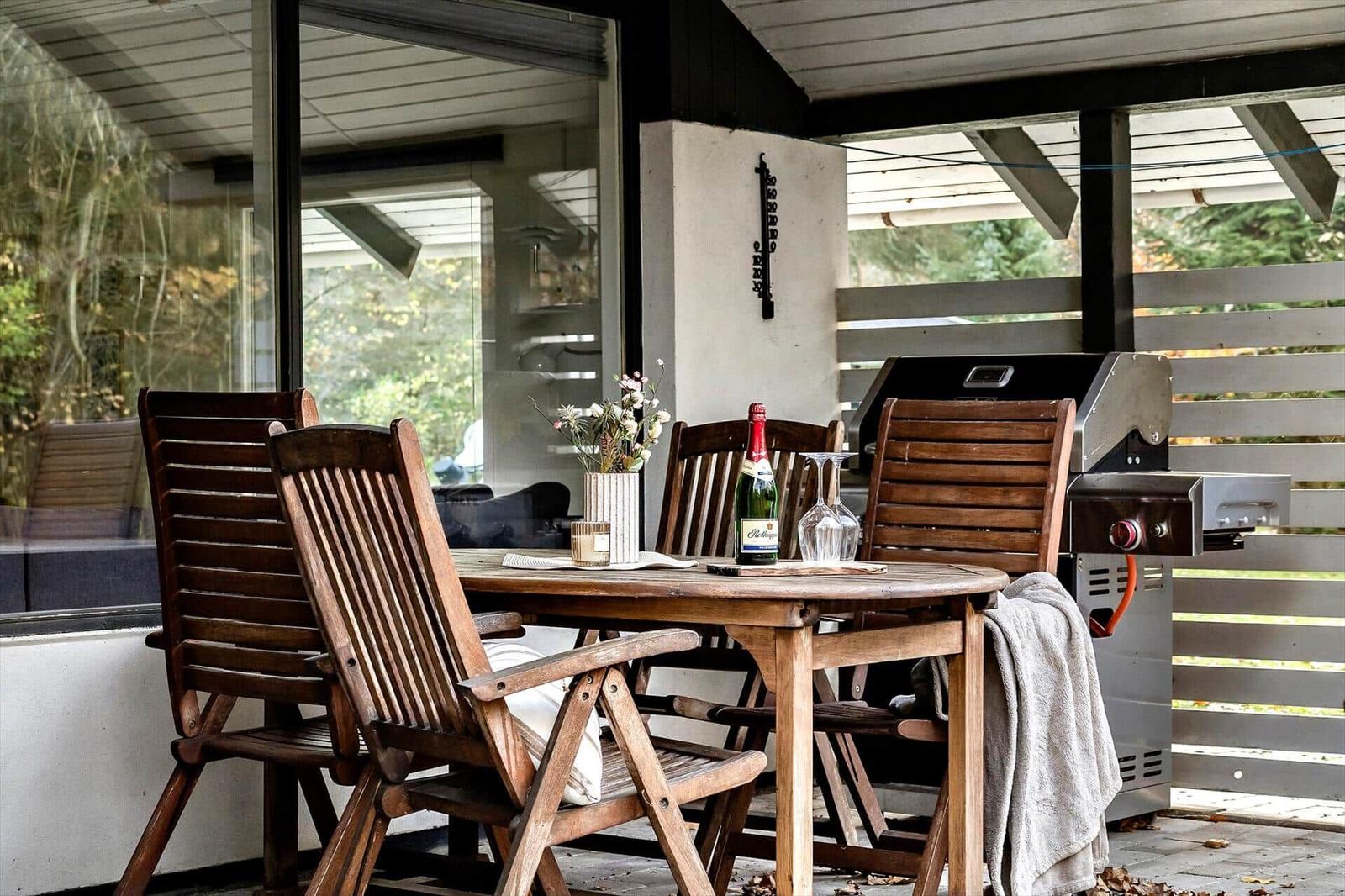 Holztisch mit Stühlen, Grill und Flasche auf Terrasse