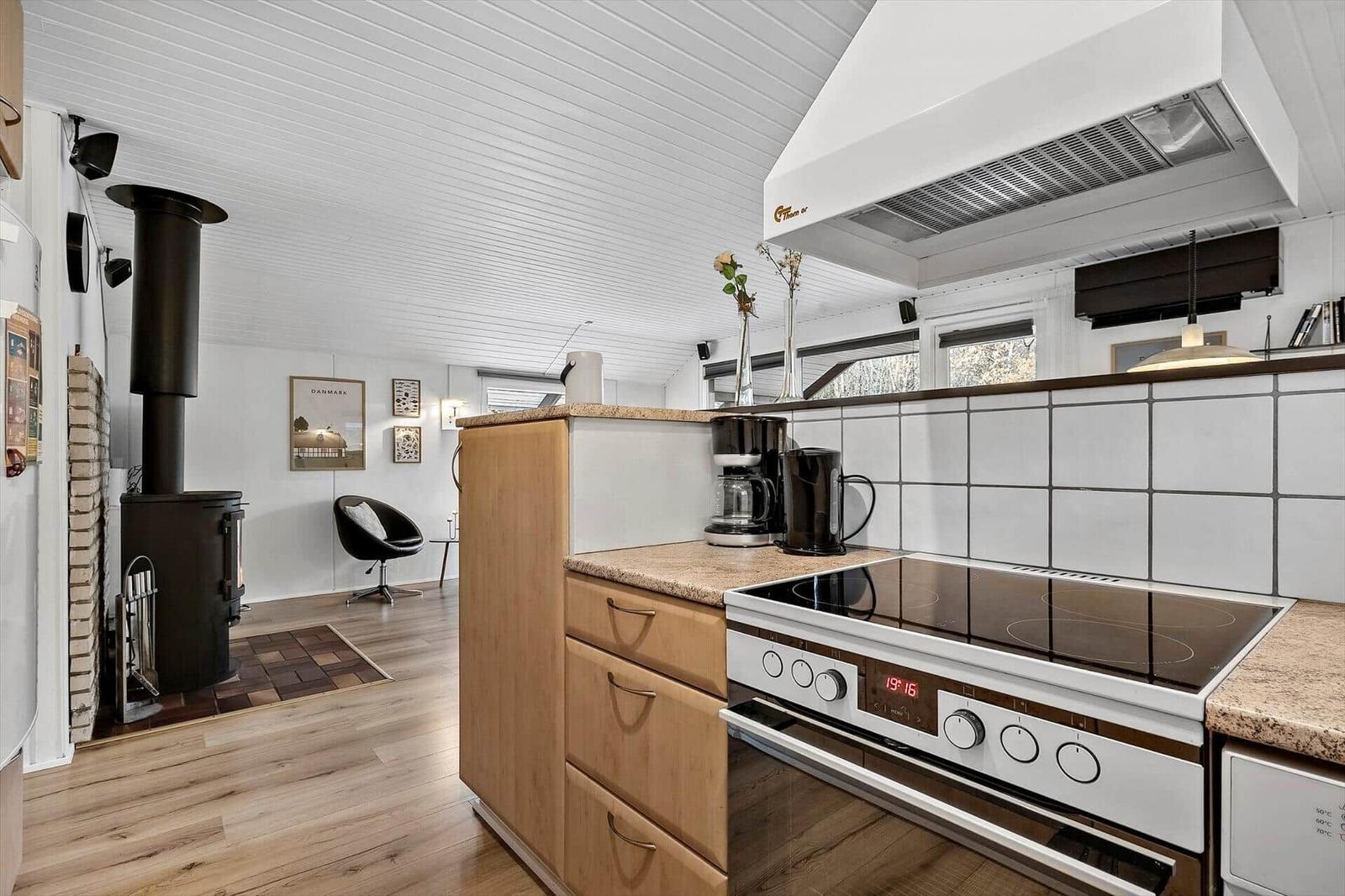 Küche mit Kochfeld, Backofen und Holzschrank. Im Hintergrund steht ein Kaminofen.