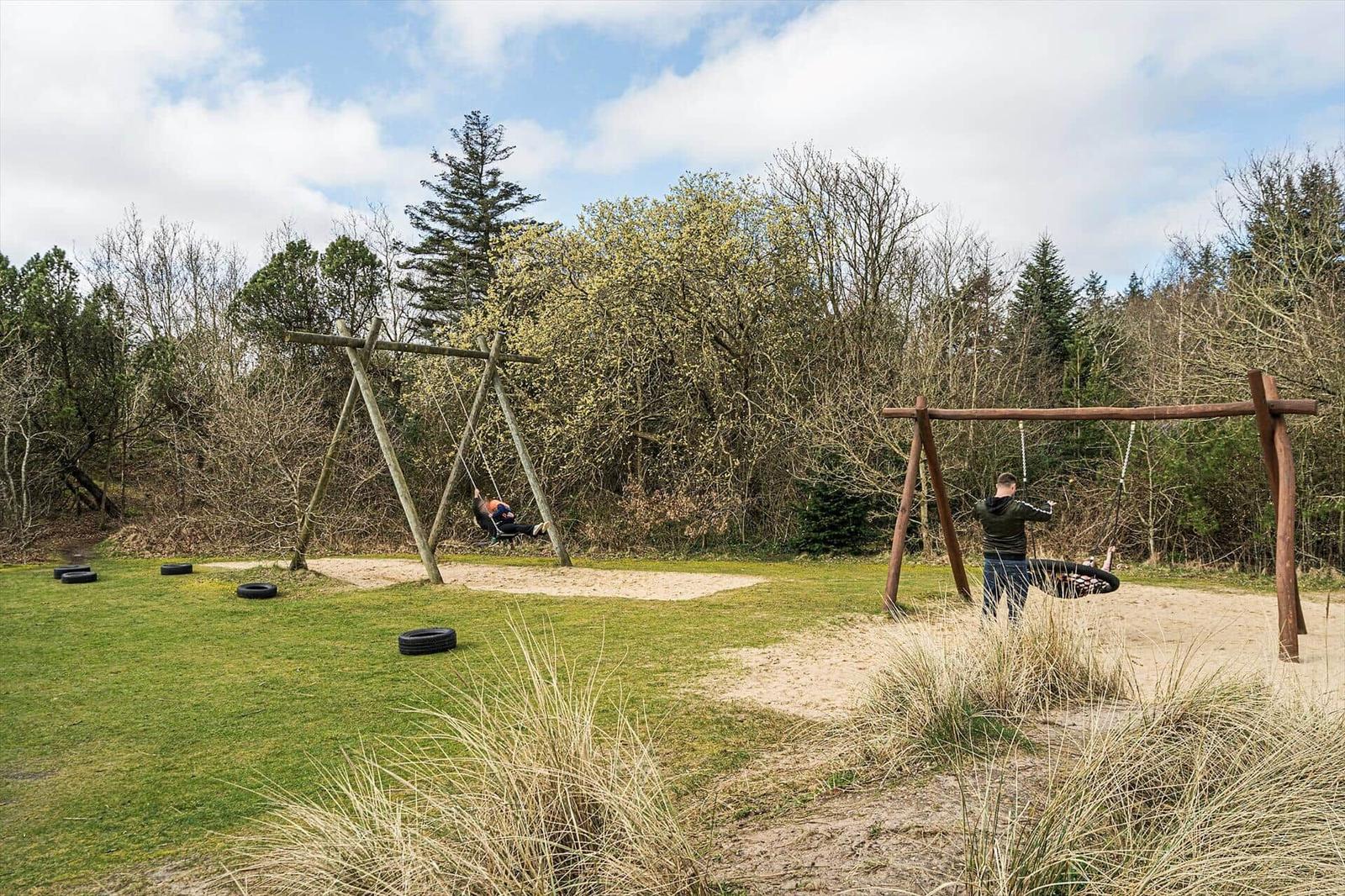 Zwei hölzerne Schaukeln mit Reifen in einem grünen Garten mit Bäumen im Hintergrund.