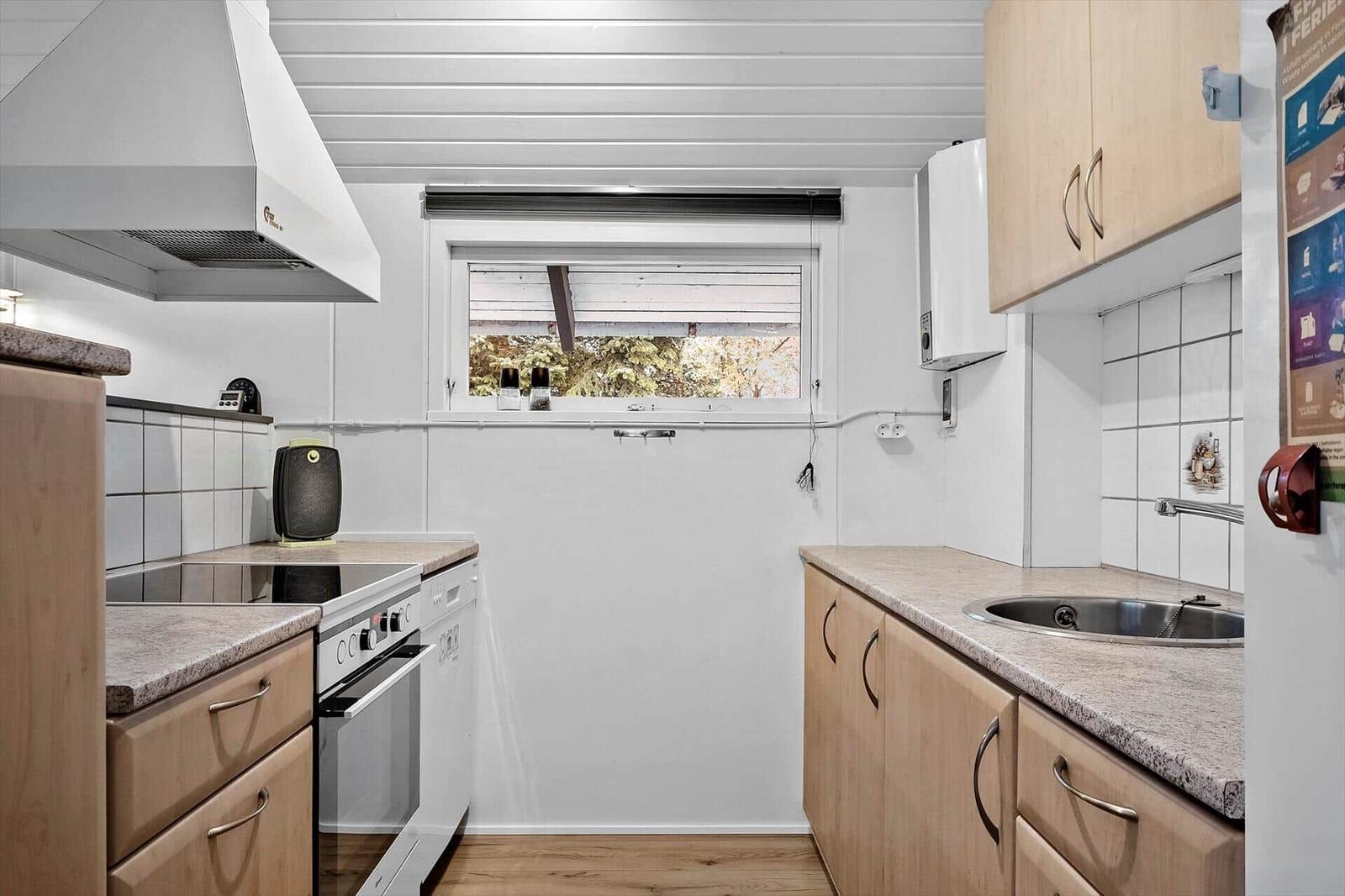 Küche mit Holzschränken, Edelstahlspüle und Fensterblick auf Bäume.