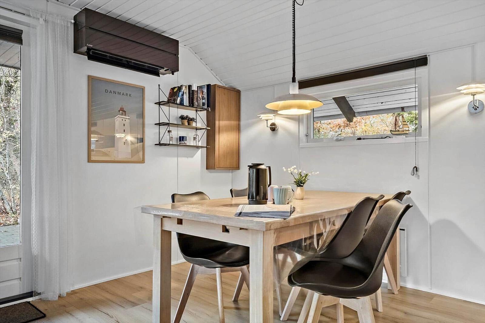 Essbereich mit Holztisch, Stühlen und Fenster. Wandbild und Regale sichtbar.