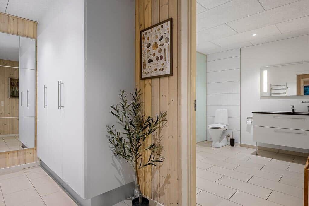 Bathroom with toilet, sink, and mirror. Wooden wall and plant visible.