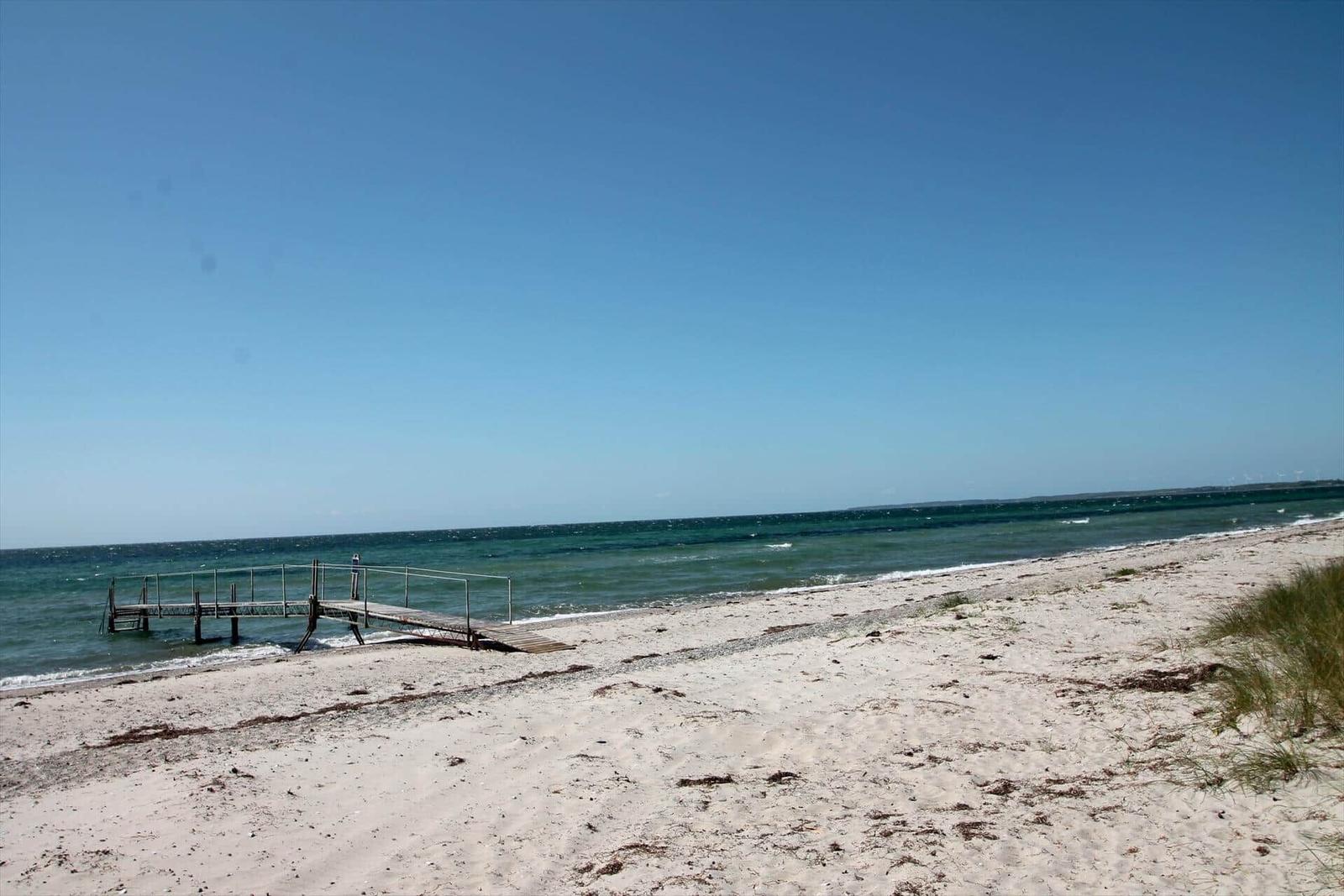 Strand mit Holzsteg und klarem Himmel. Sandstrand mit Wellen.