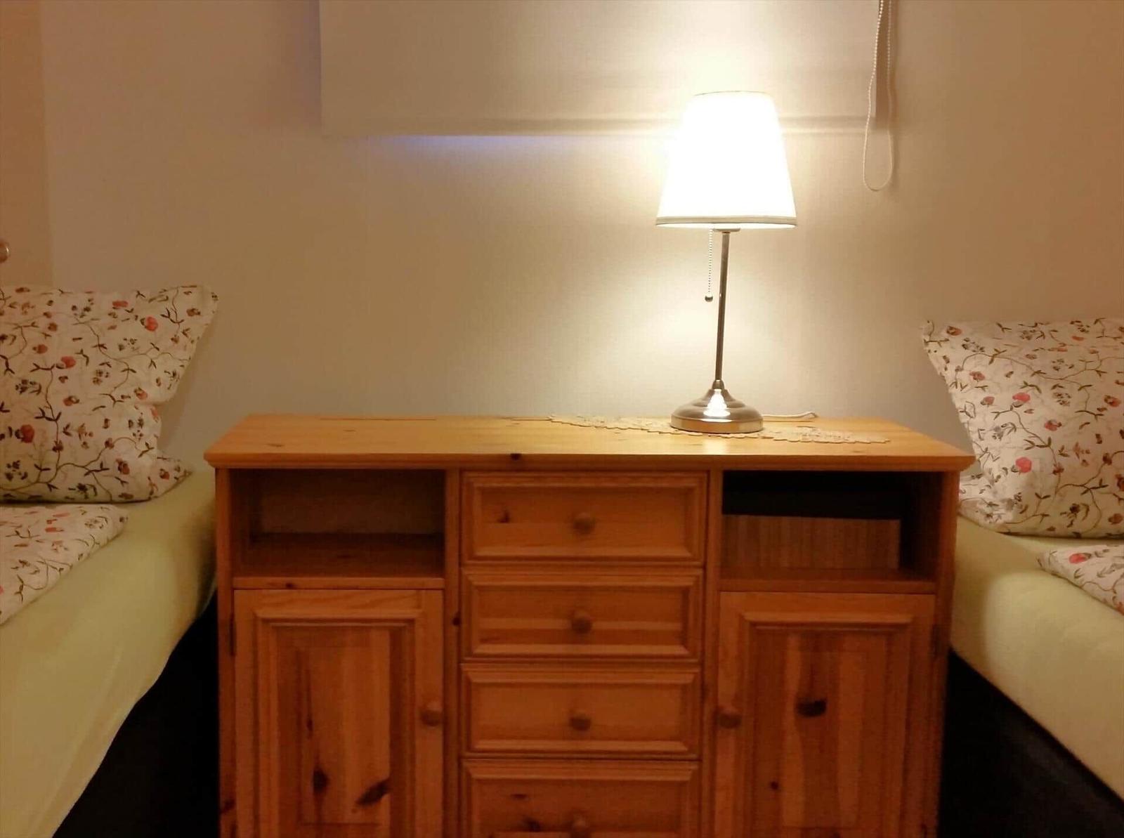 Zwei Betten flankieren einen Holzschrank mit Lampe.