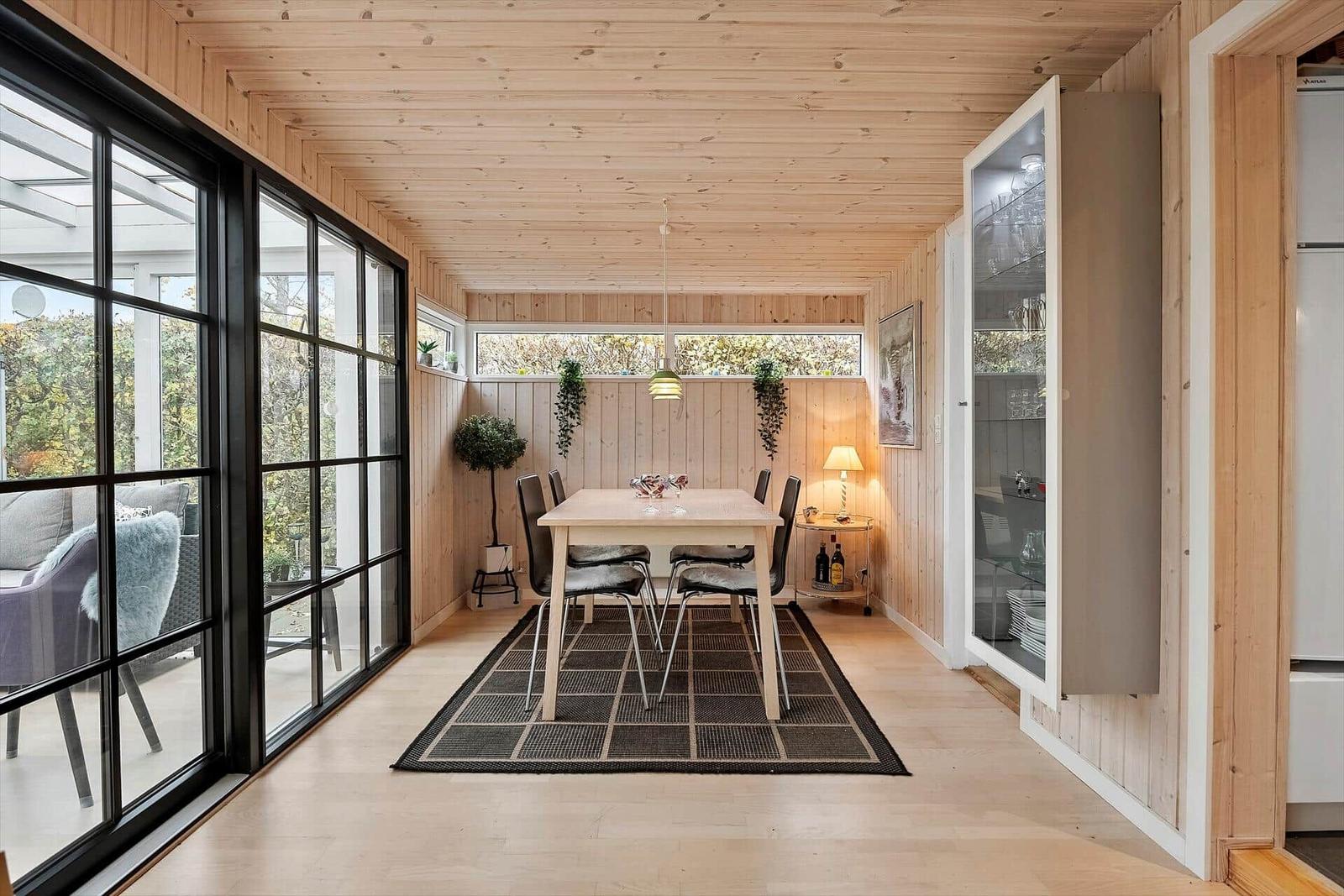 Esszimmer mit Holzwand, Tisch, Stühlen und Glaswand zur Terrasse.