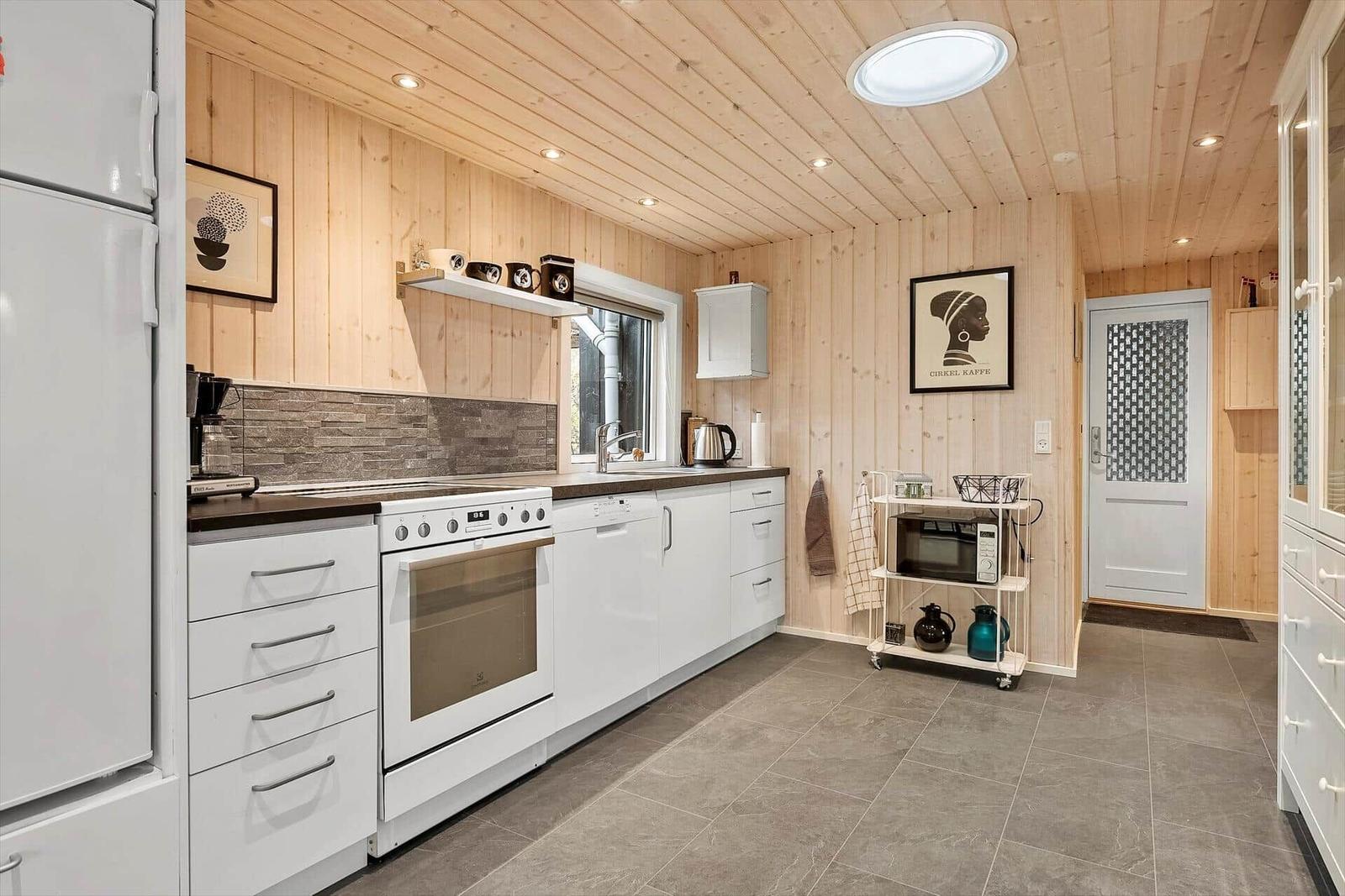 Küche mit weißen Schränken, Holzwand und Arbeitsplatte. Mikrowelle und Kühlschrank sind vorhanden.
