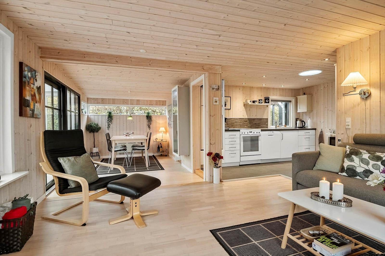 Wohnzimmer mit Essbereich und Küche. Holzwände und -decke. Sofa, Sessel und Tisch.
