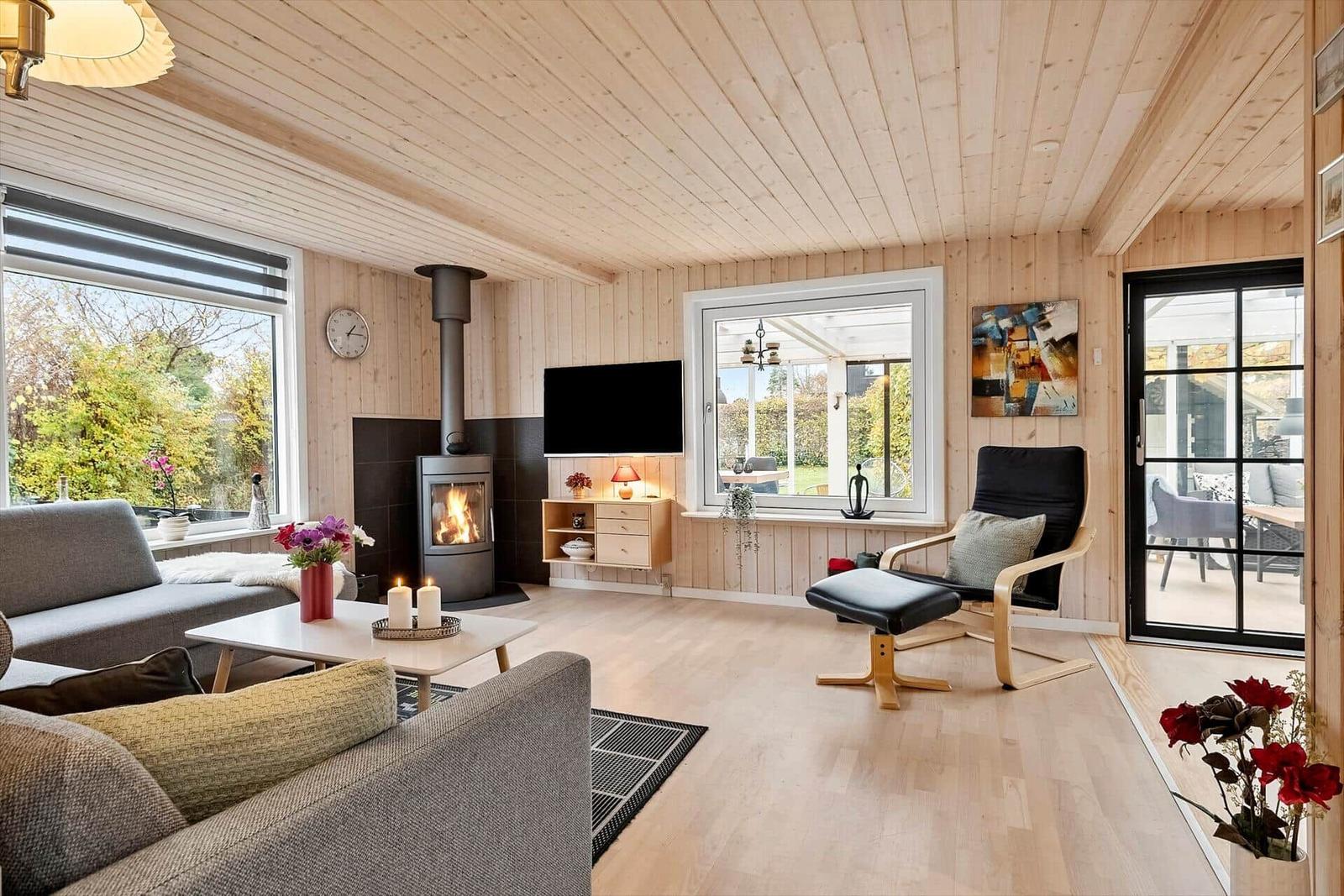 Wohnzimmer mit Kamin, Sofa, Fernseher und Sitzgelegenheit. Holzwände und Boden.