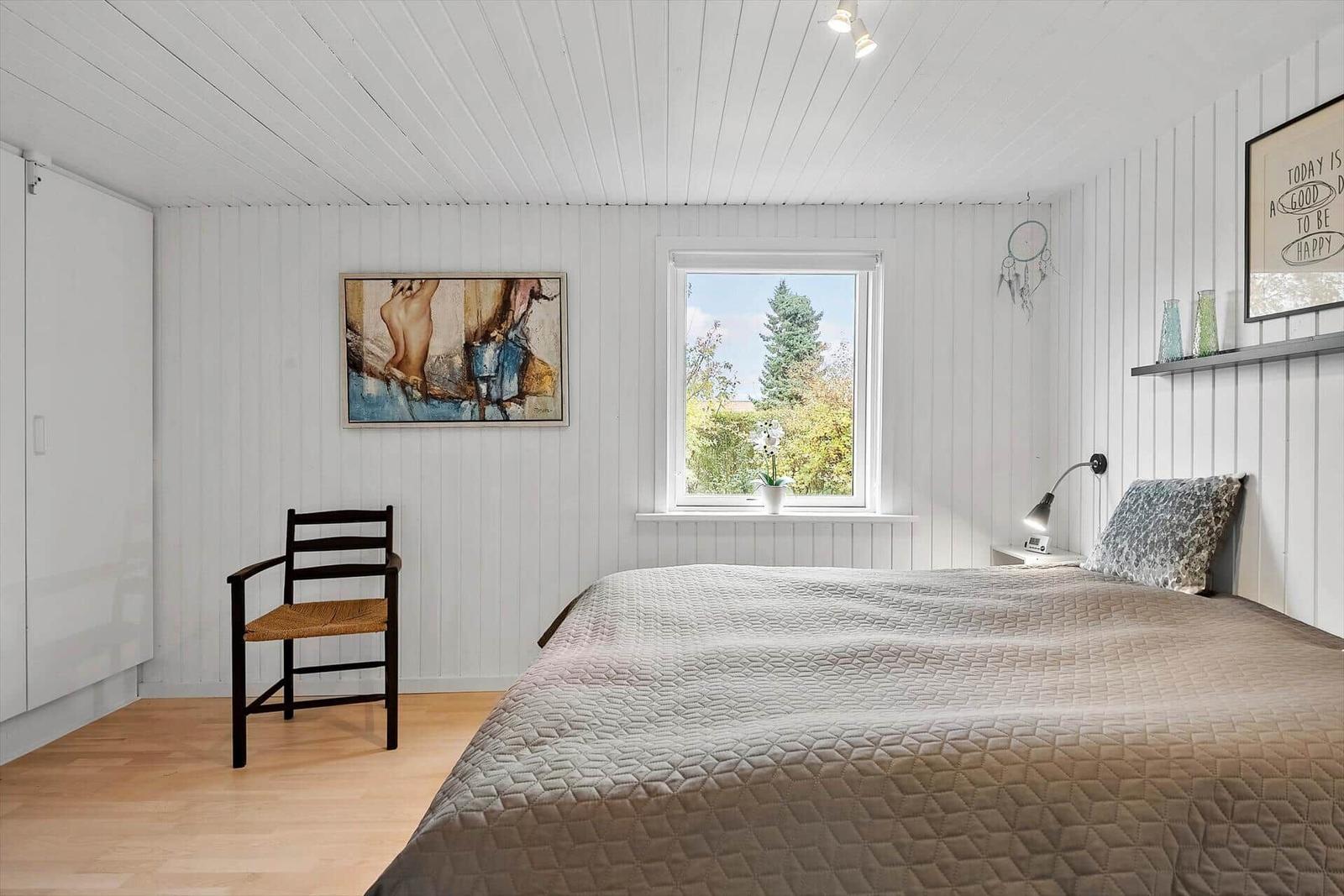 Schlafzimmer mit Bett, Stuhl und Fenster mit Blick auf Grünflächen.