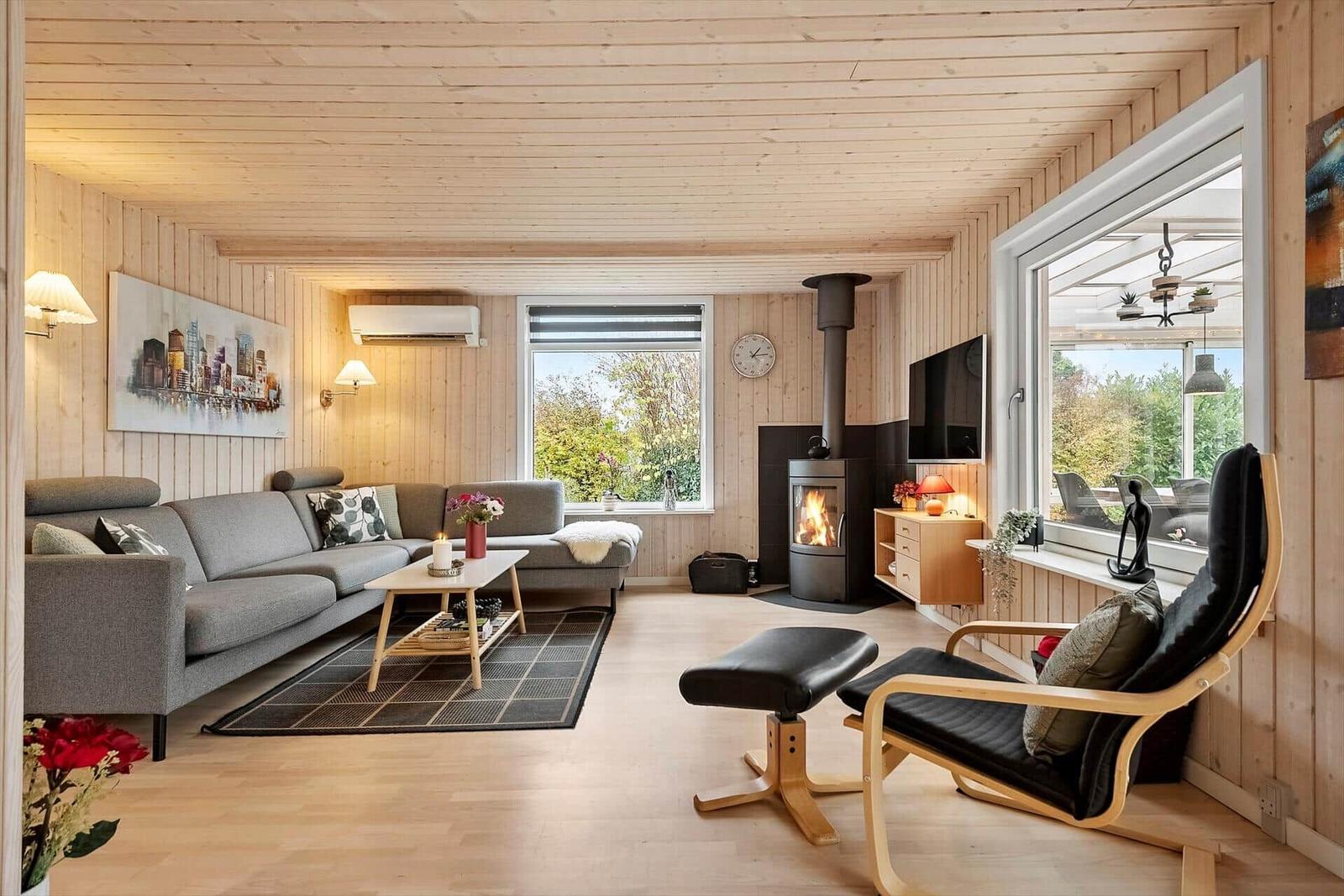 Wohnzimmer mit Holzwand, Sofa, Kamin und Sessel. Fenster zeigen Garten.
