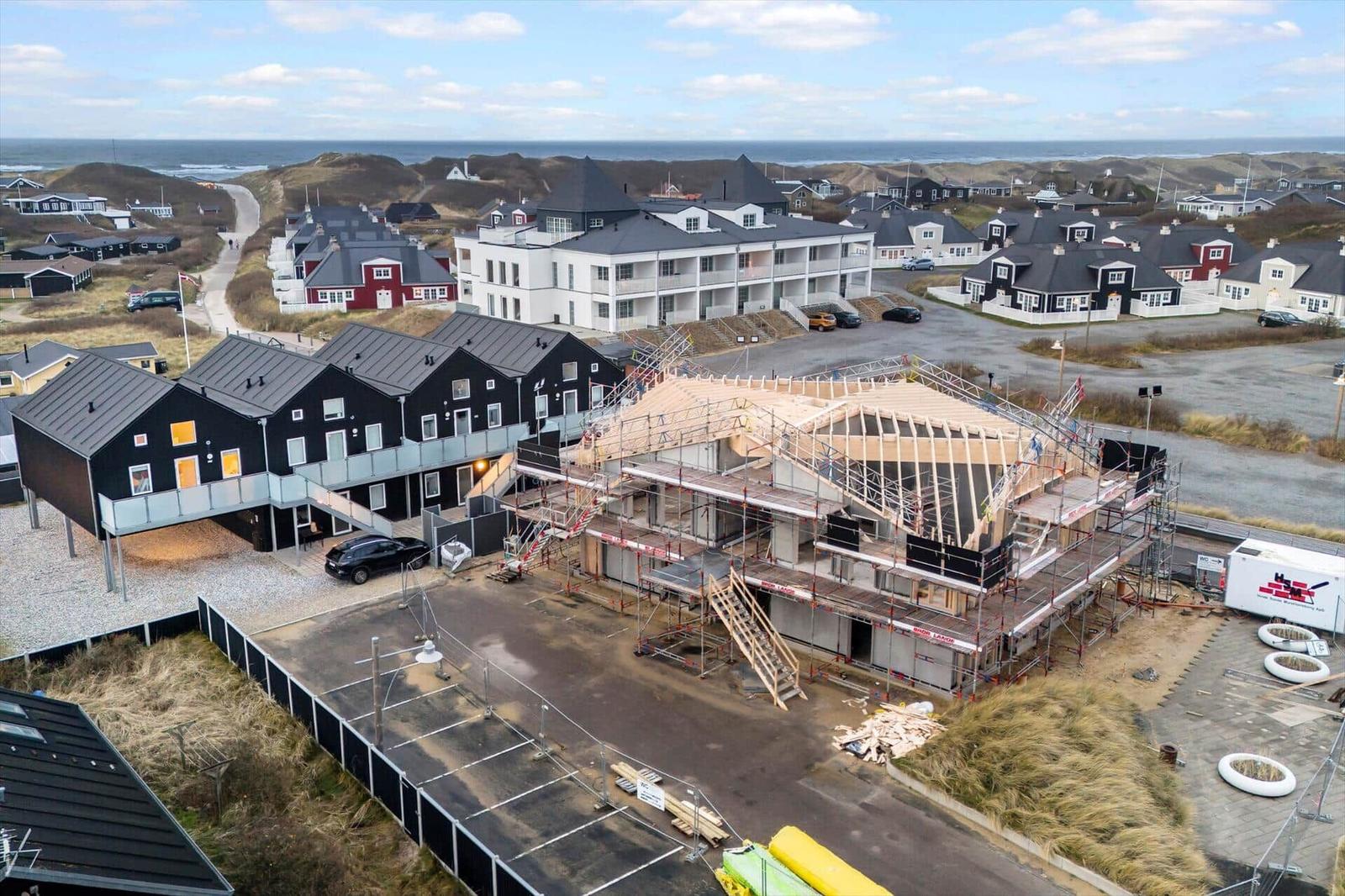 Neubau mit Scaffolding in Strandnähe, umgeben von Häusern und Dünen.
