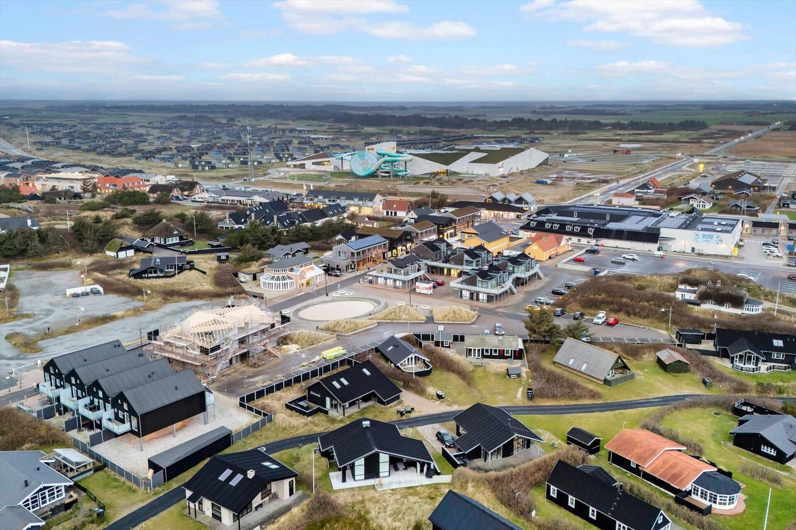 Aerial view of a coastal village with houses, a water park, and open fields.