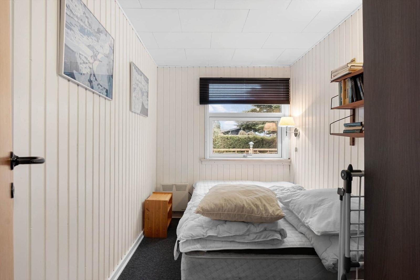 Schlafzimmer mit Bett, Fenster und Bücherregal an der Wand.
