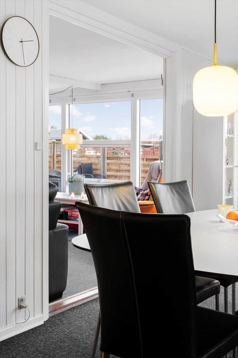Essbereich mit schwarzen Stühlen und weißem Tisch. Durchgang zum Wohnbereich mit großem Fenster.