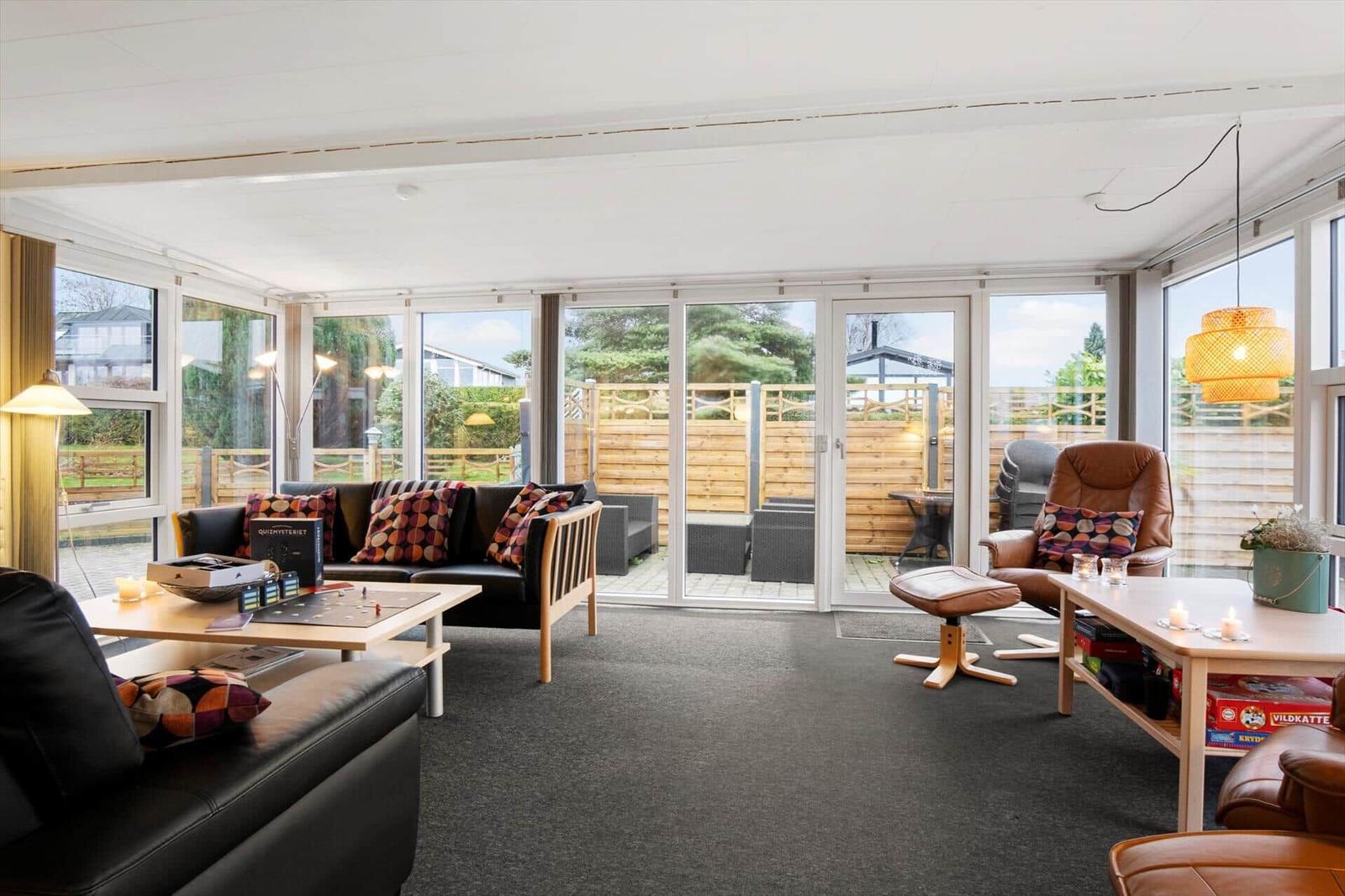 Wohnraum mit Sofa, Sessel und Tischen. Durchgehende Glasfront zum Garten.
