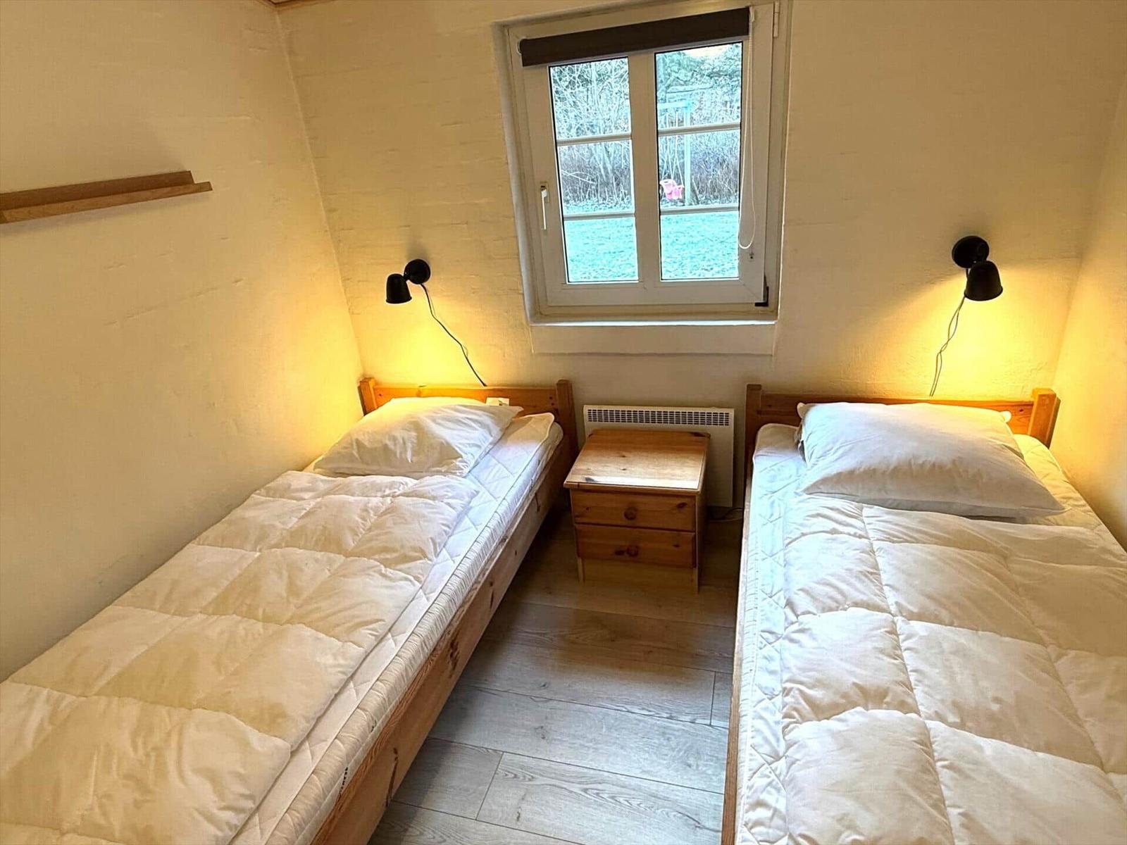 Zwei Einzelbetten mit Nachttisch und Fenster im Zimmer.