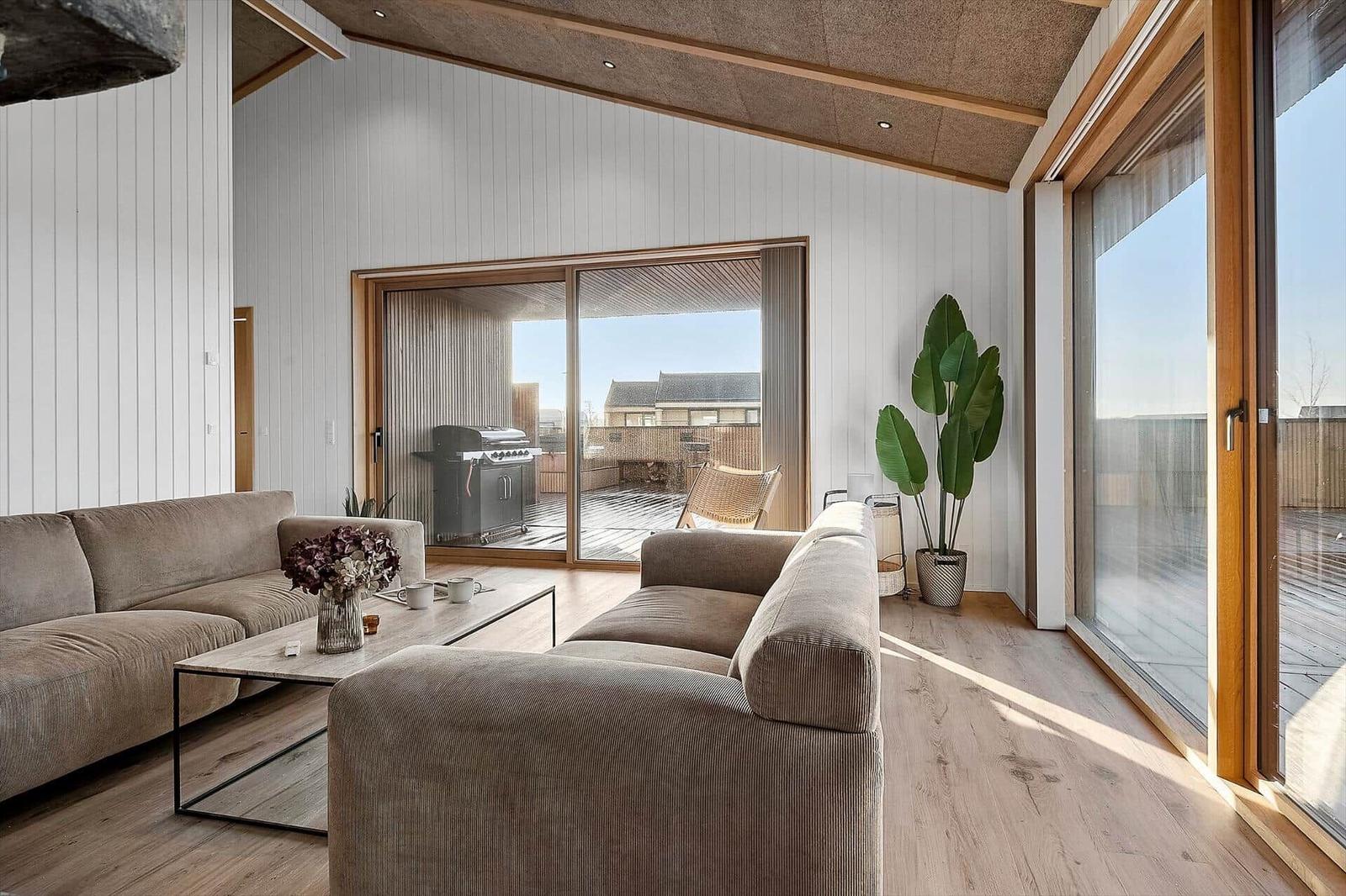 Wohnzimmer mit Sofa, Tisch und Blick auf Terrasse mit Grill.