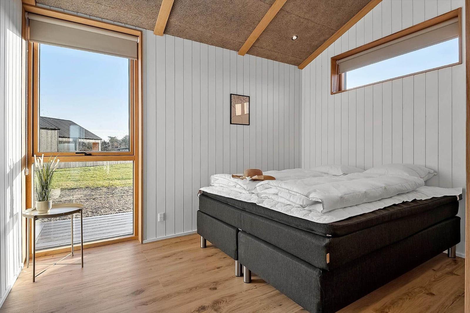 Schlafzimmer mit großem Fenster, Bett und Holzboden.