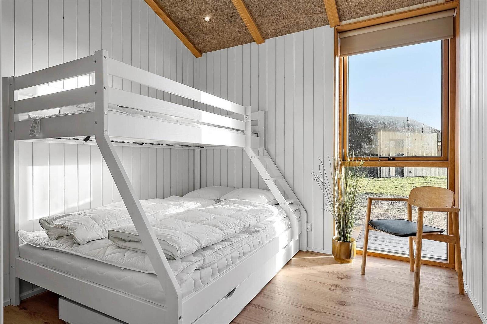 Schlafzimmer mit Doppelstockbett, Holzboden und großem Fenster.