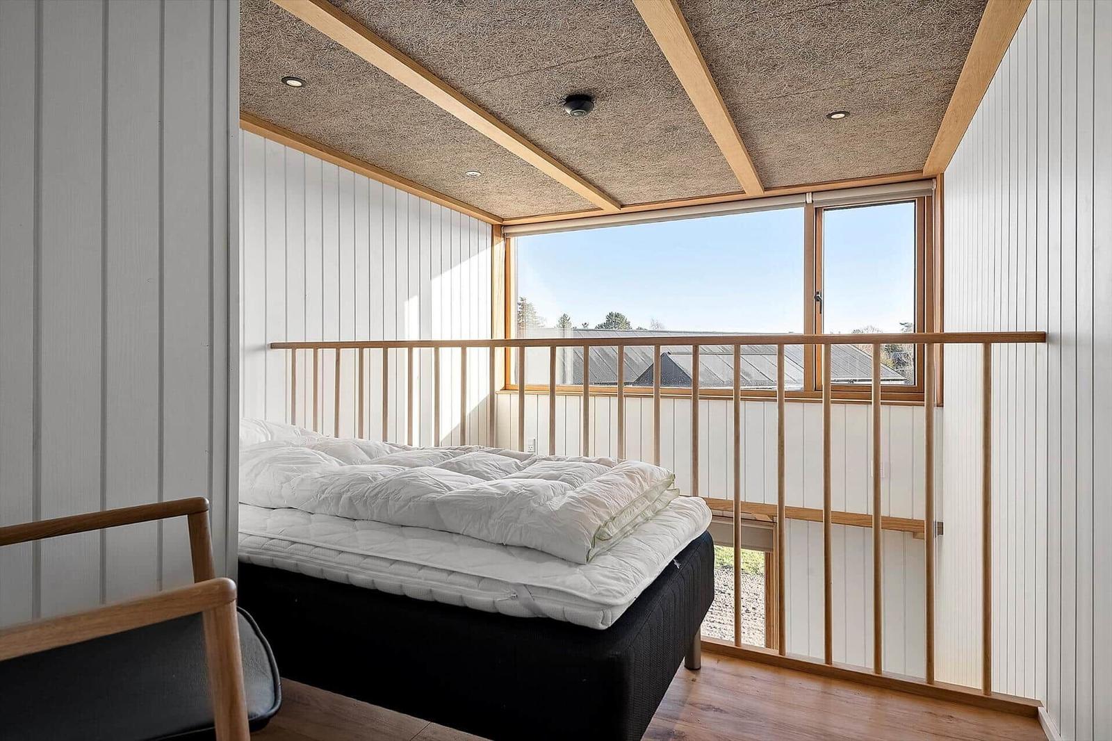 Schlafzimmer mit Bett, Holzbalken und großem Fenster mit Blick nach draußen.