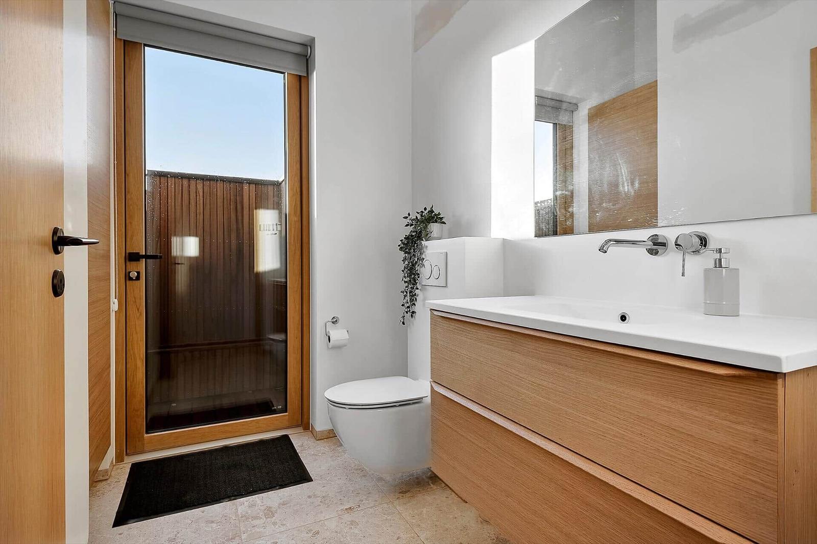 Badezimmer mit Waschtisch, Toilette und Glasfront zur Terrasse.