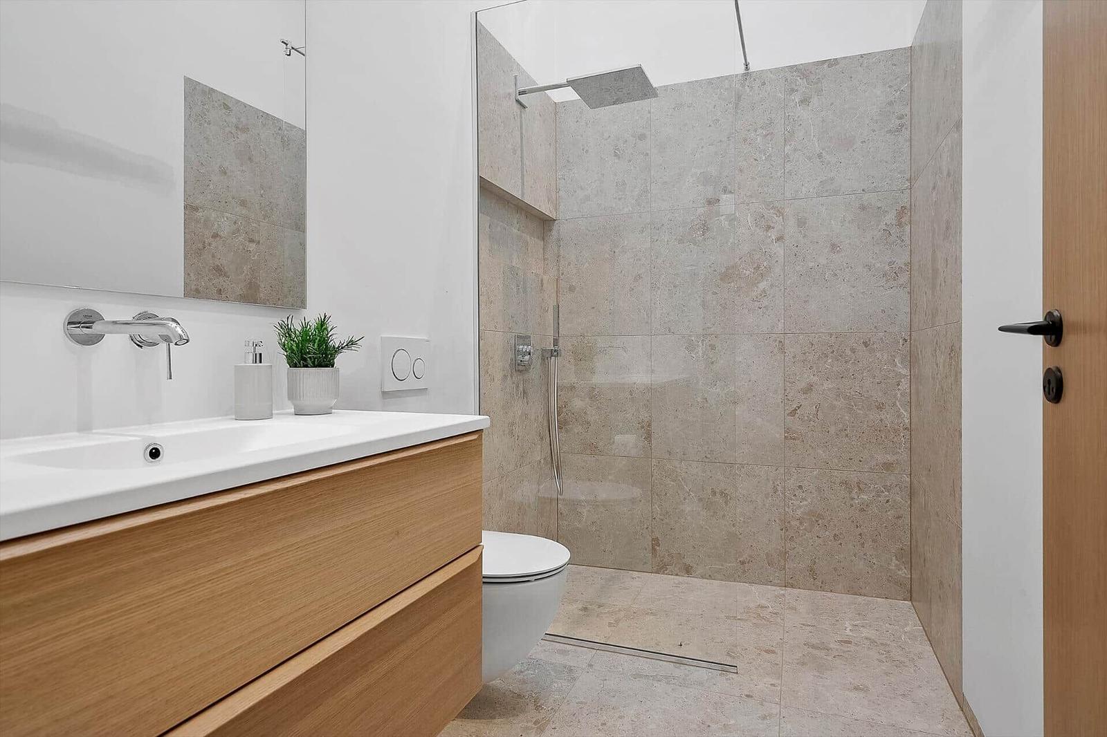 Bad mit Dusche, Waschbecken und Toilette. Holzunterschrank und Spiegel.