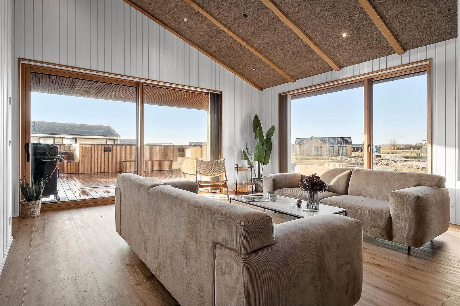 Wohnraum mit zwei Sofas, Holzboden und großen Fenstern zur Terrasse.