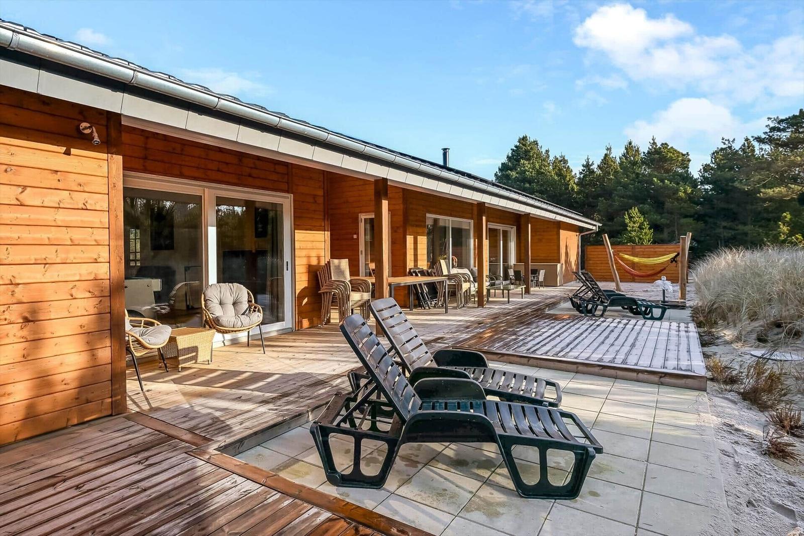 Wooden house with terrace, sun loungers, and view of forest.