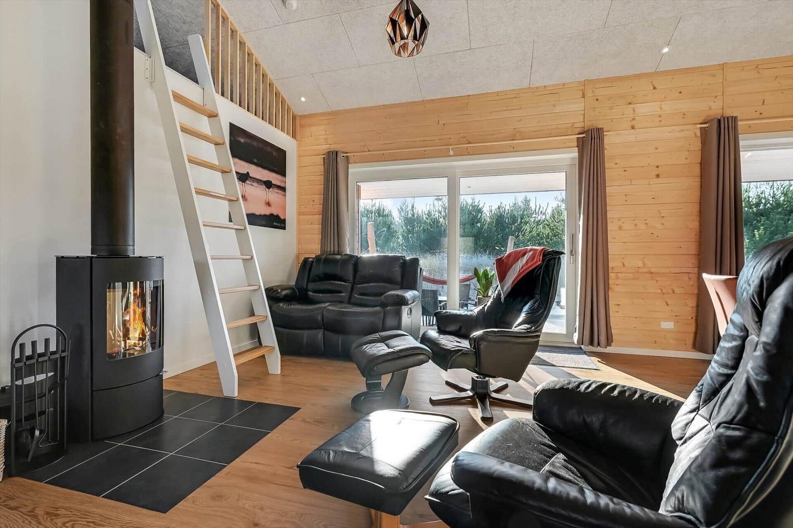 Living room with fireplace, black chairs, and wooden walls. Stairs to upper level.