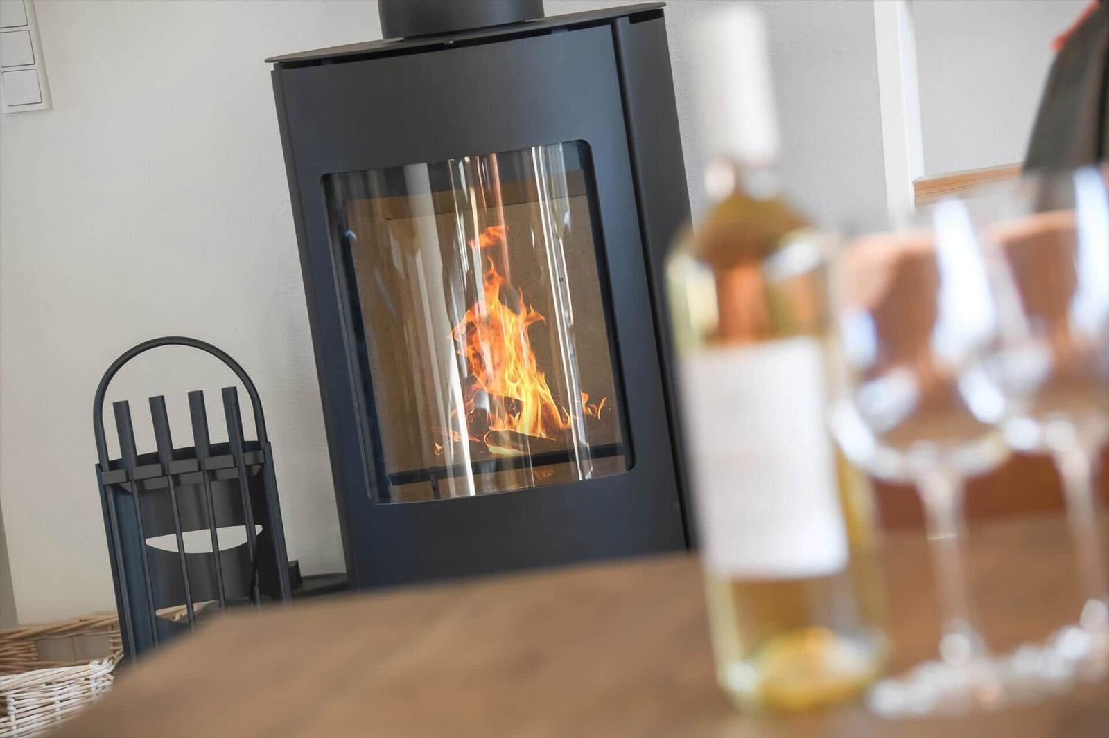 A wood-burning stove with fire. On the table, a glass and a bottle.