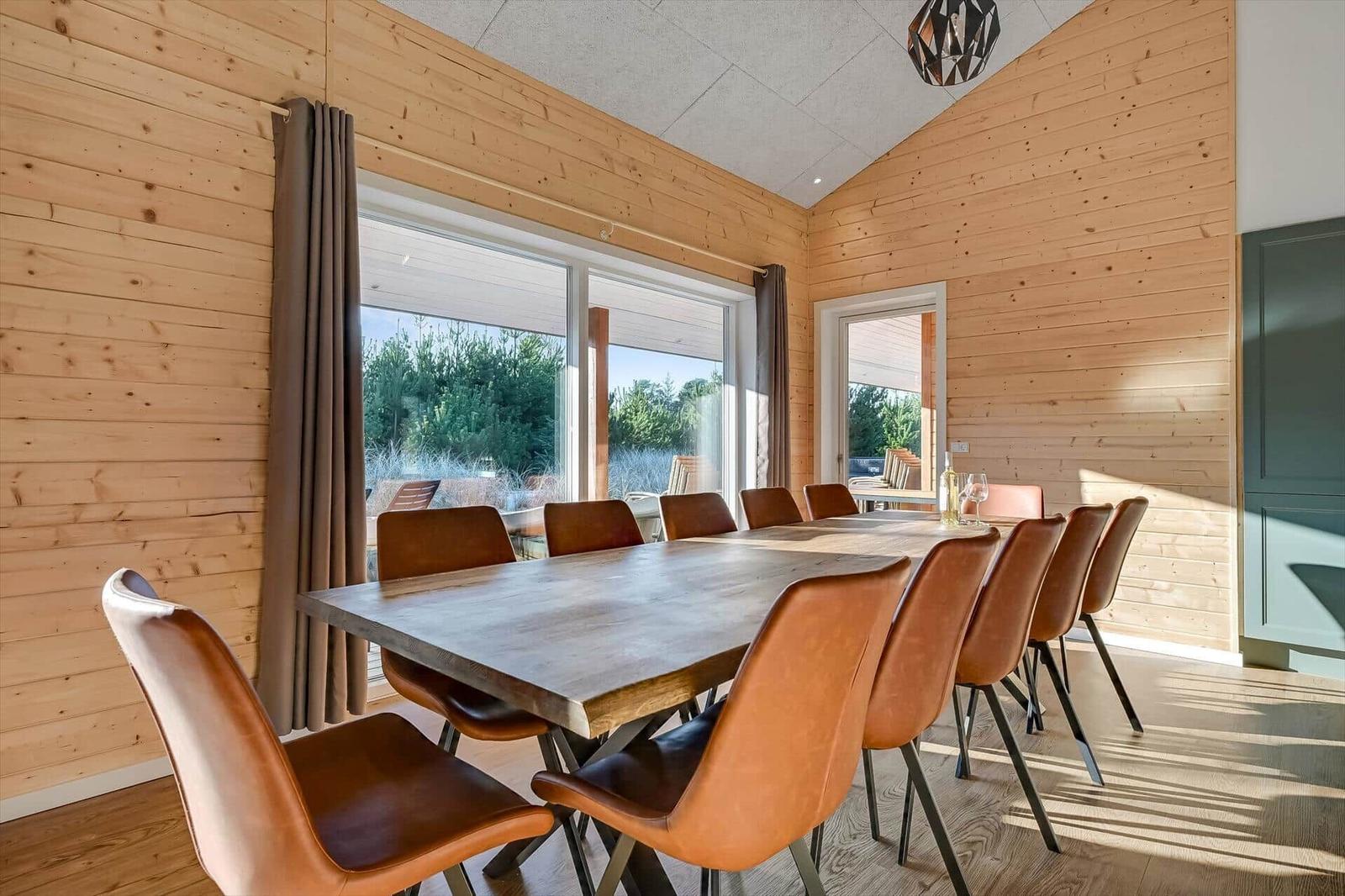 Dining room with wooden walls, large table and brown chairs. Large windows with view of garden.
