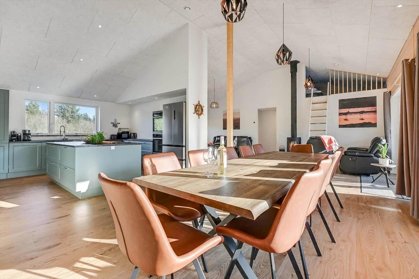 Dining area with wooden table and leather chairs. Kitchen with island and view of nature.