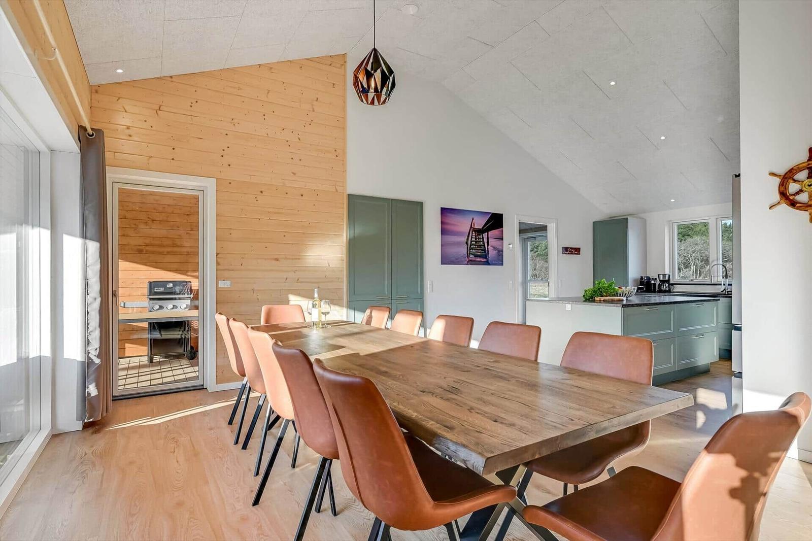 Large dining area with wooden table and brown chairs. Kitchen and grill area are visible.