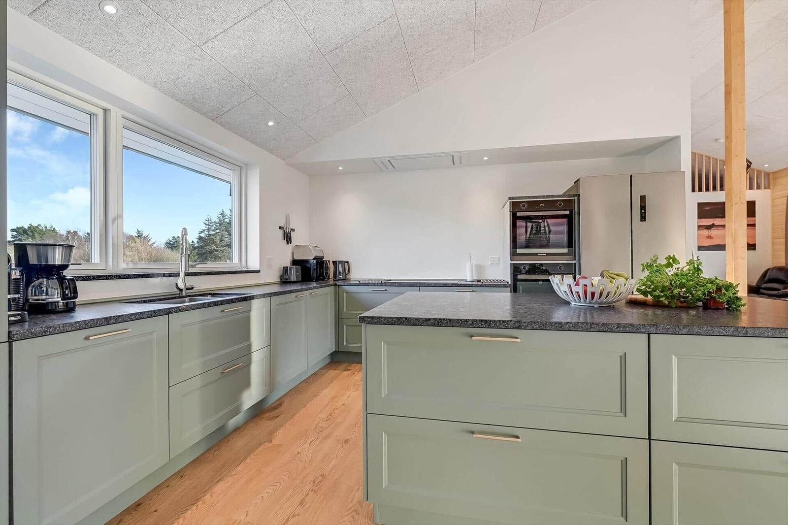 Modern kitchen with green cabinets, stone countertops, and view of nature.