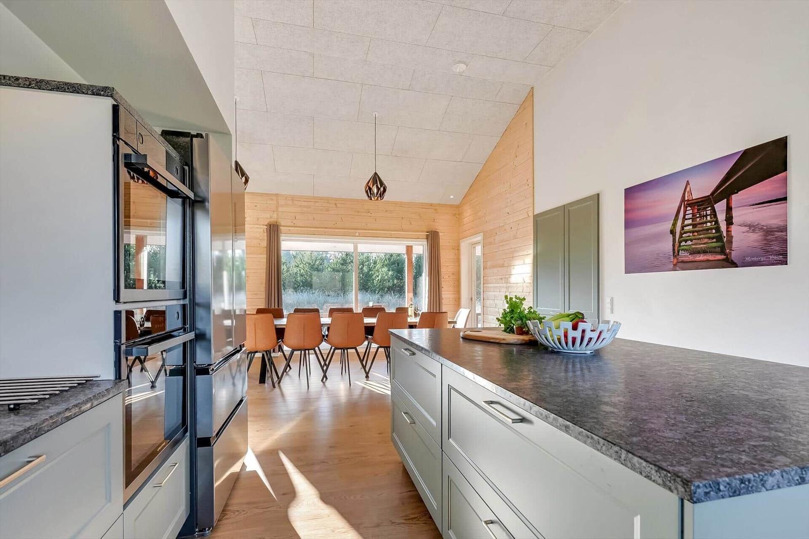 Modern kitchen with dining area and wooden wall. Refrigerator, range hood, and kitchen island.