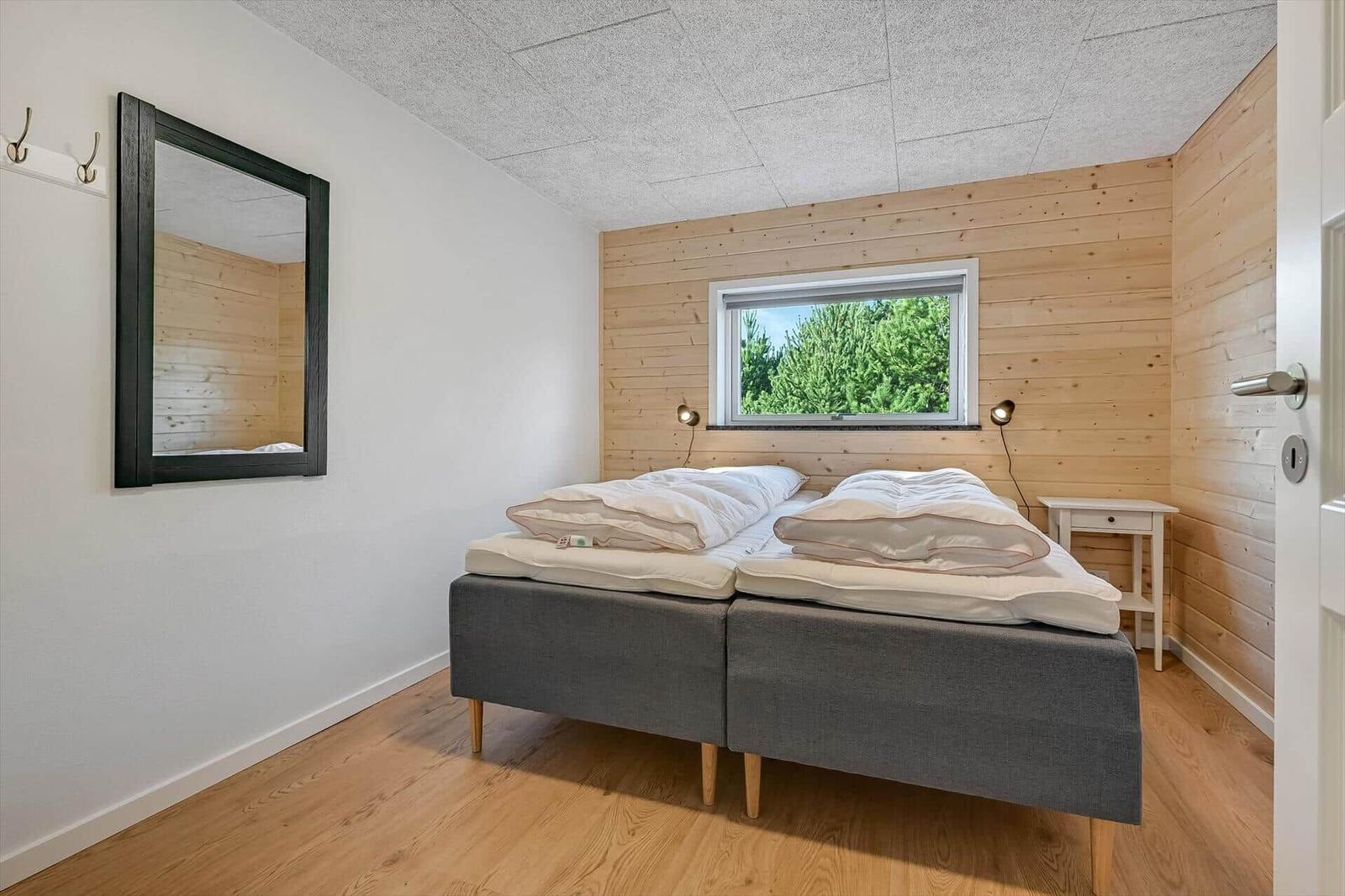Bedroom with double bed, wooden wall, and window with view of trees.