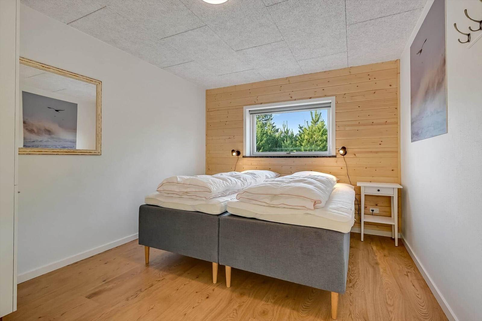 Bedroom with double bed, wooden wall, and window with forest view.