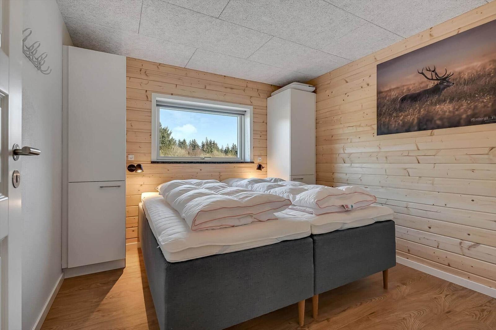 Bedroom with bed, window, and wooden wall. Wall picture of a deer.