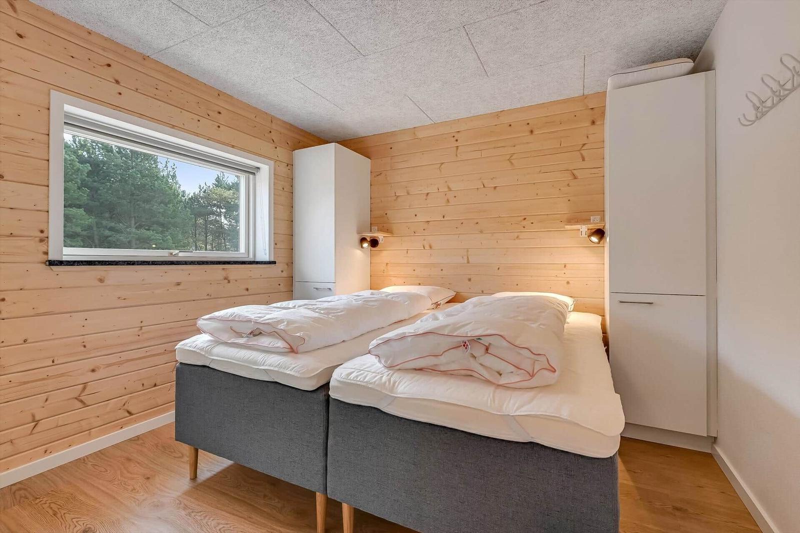 Bedroom with double bed, wooden wall, and window with forest view.
