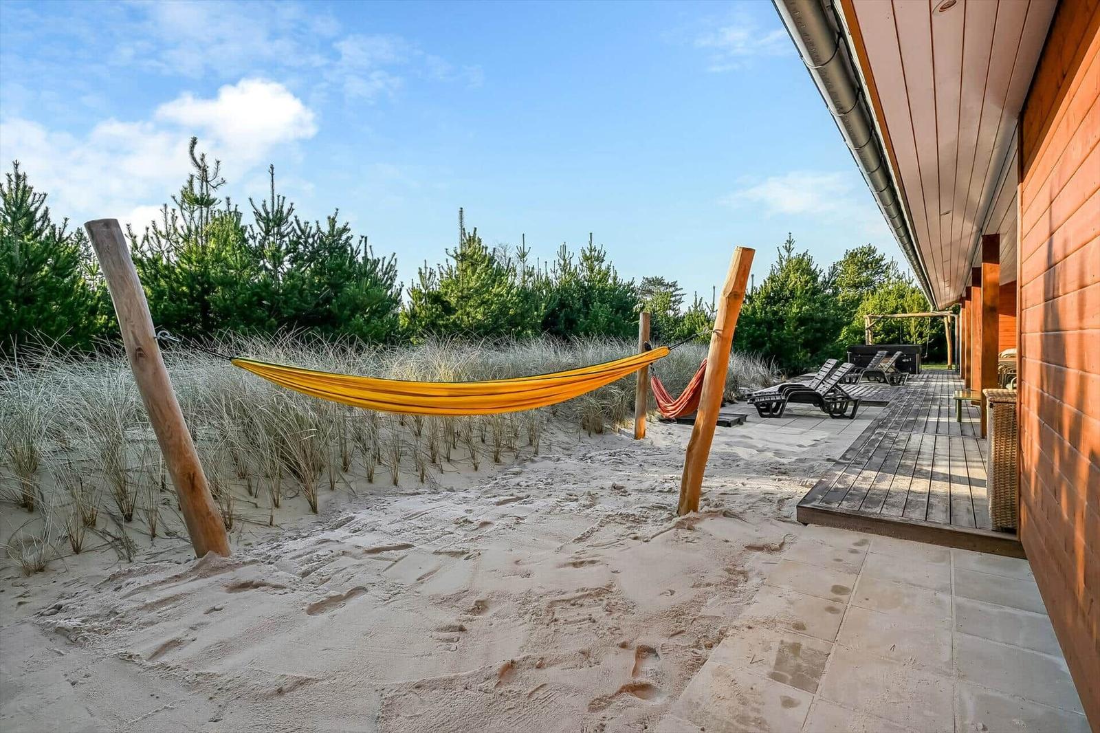 Sandy terrace with hammocks and sun loungers next to wooden house.