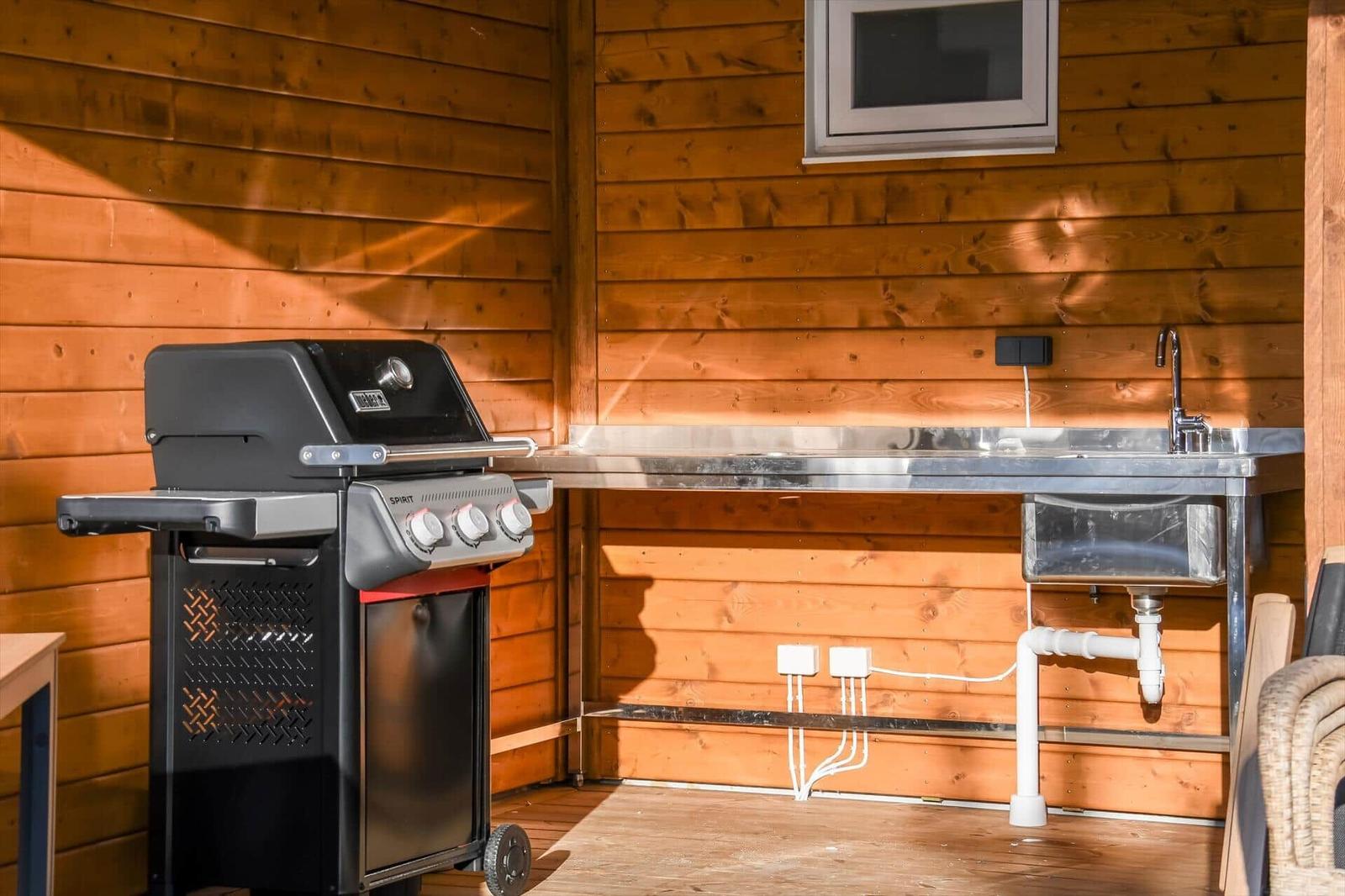 Outdoor kitchen with grill and stainless steel sink against wooden wall