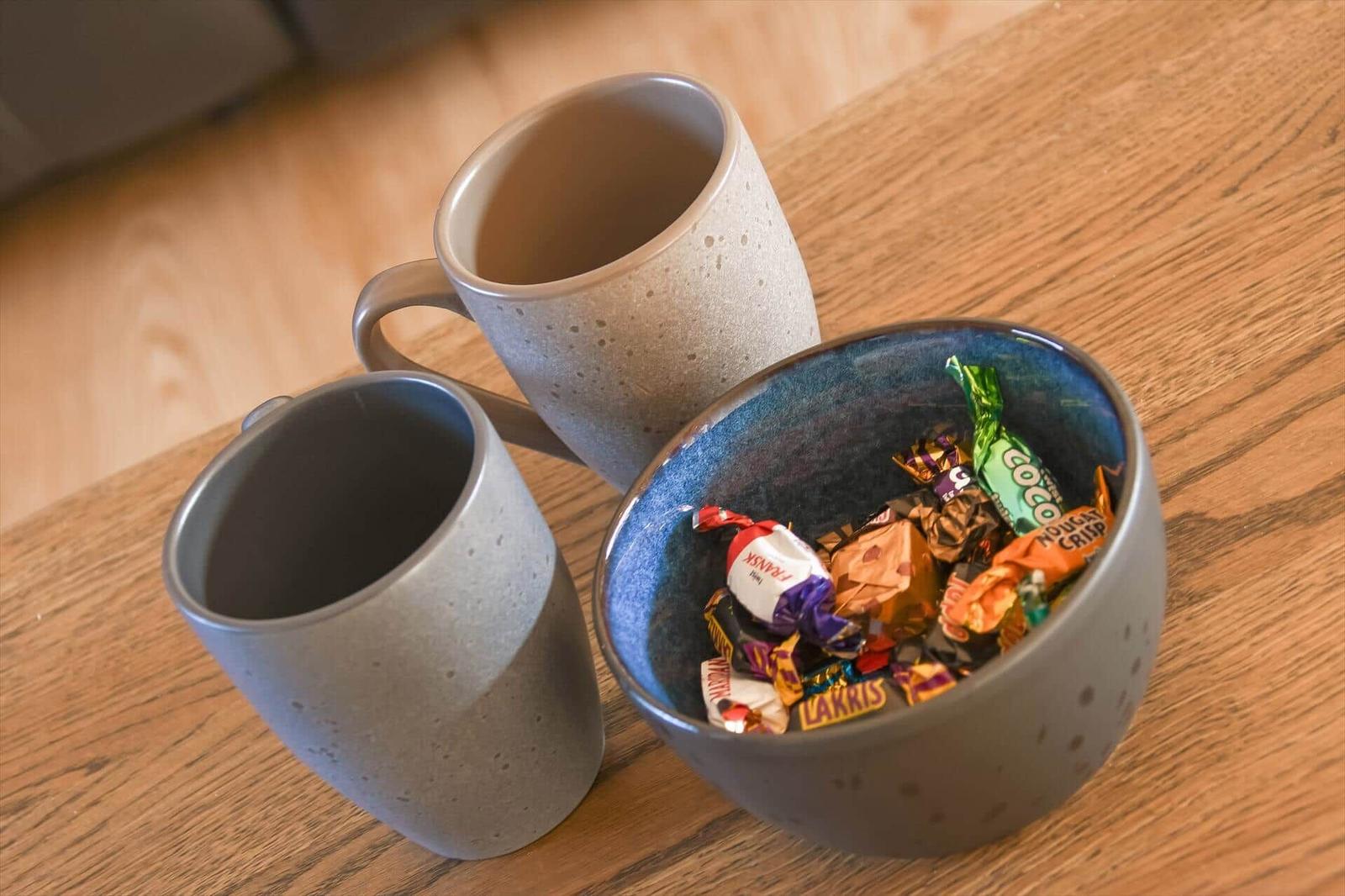 Two mugs and a bowl with sweets on wooden table.