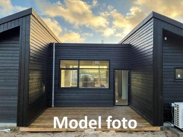 Modern wooden house with large window and deck under cloudy sky.