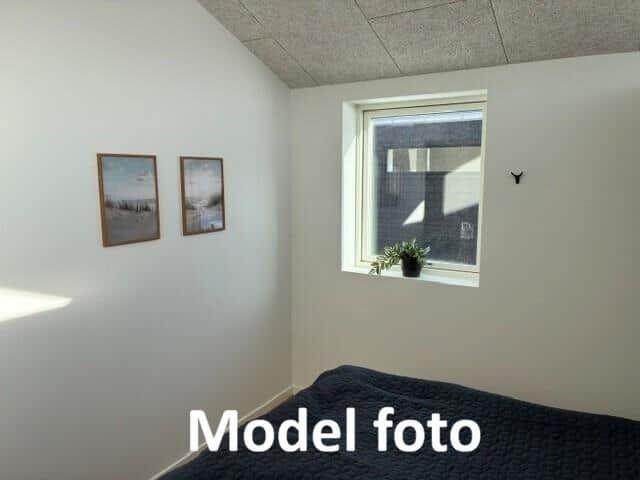 Bedroom with window, two pictures on the wall, and a bed with dark bedding.