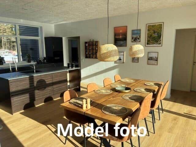 Dining area with wooden table, chairs, and kitchen island in background.