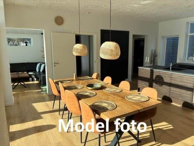Dining area with wooden table, chairs, and pendant lamps. Kitchen and living room in background.